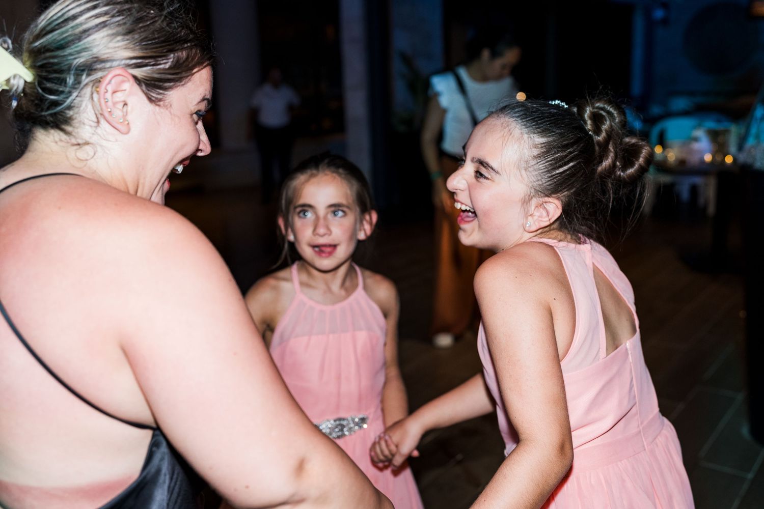 Young girls in pink dresses laughing and dancing together at a wedding reception celebration.