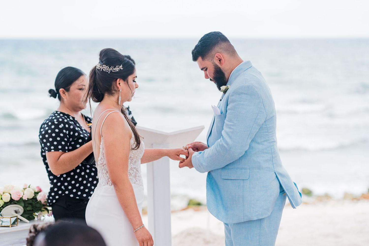Bride and groom exchanging rings during a romantic beach wedding ceremony by the ocean.