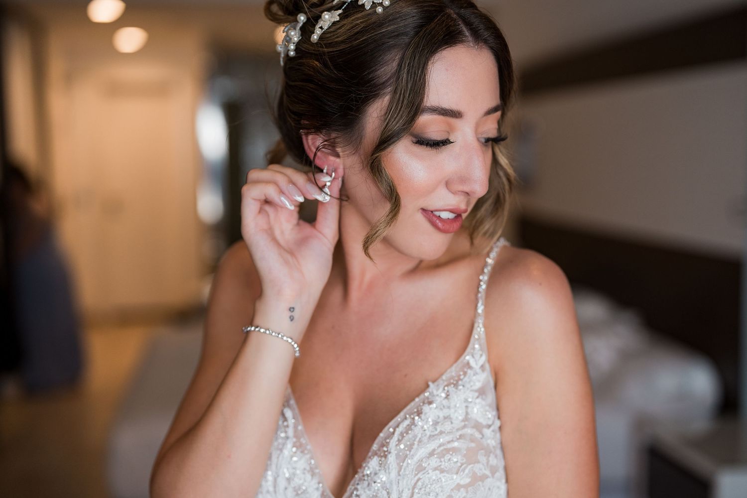 Bride putting on earring in wedding dress with floral hair accessory.