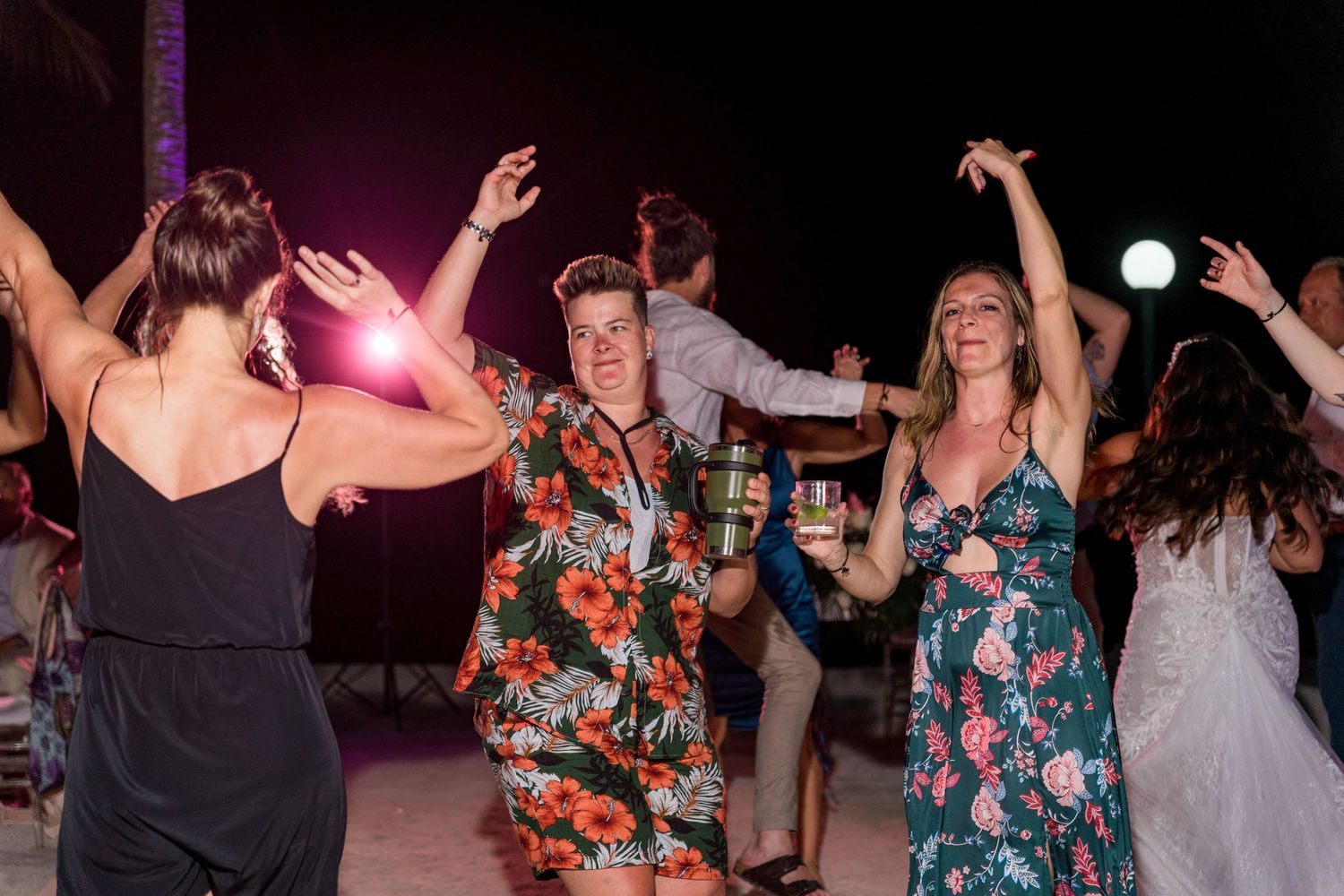 Wedding guests in colorful attire dance joyfully together at an outdoor nighttime beach reception.
