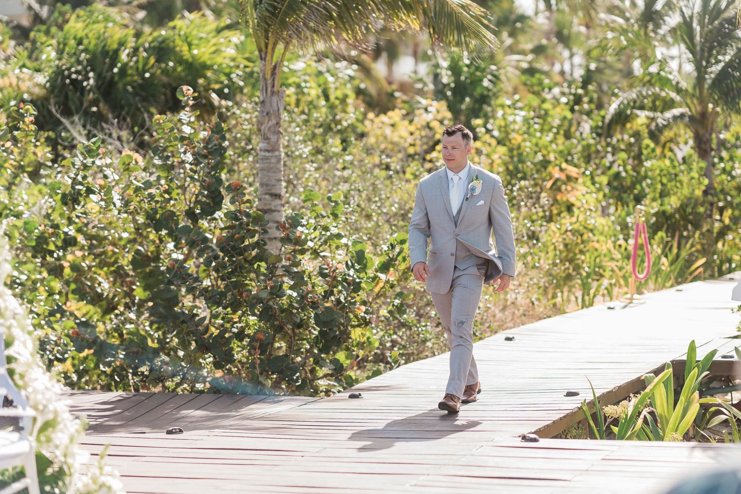 Groom in light gray suit walking on wooden boardwalk at grand palladium costa mujeres wedding