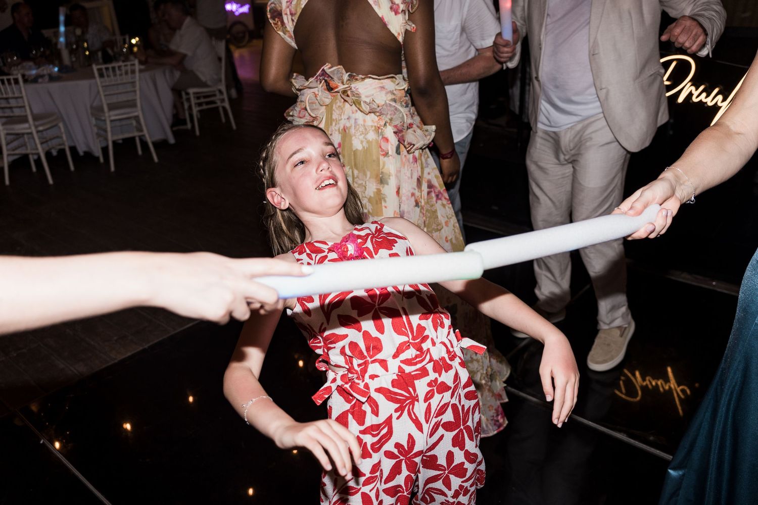 Young girl in floral dress laughing and dancing at a wedding reception party on a dark dance floor.