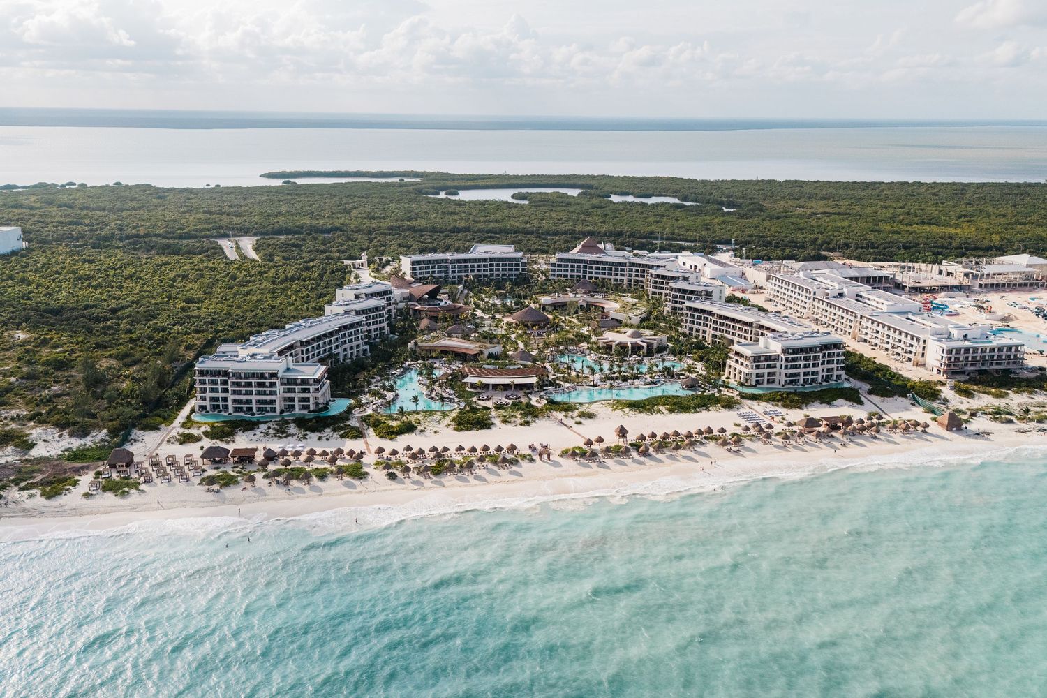 Aerial view of a luxury beachfront resort with pools, surrounded by lush greenery and turquoise Caribbean waters.