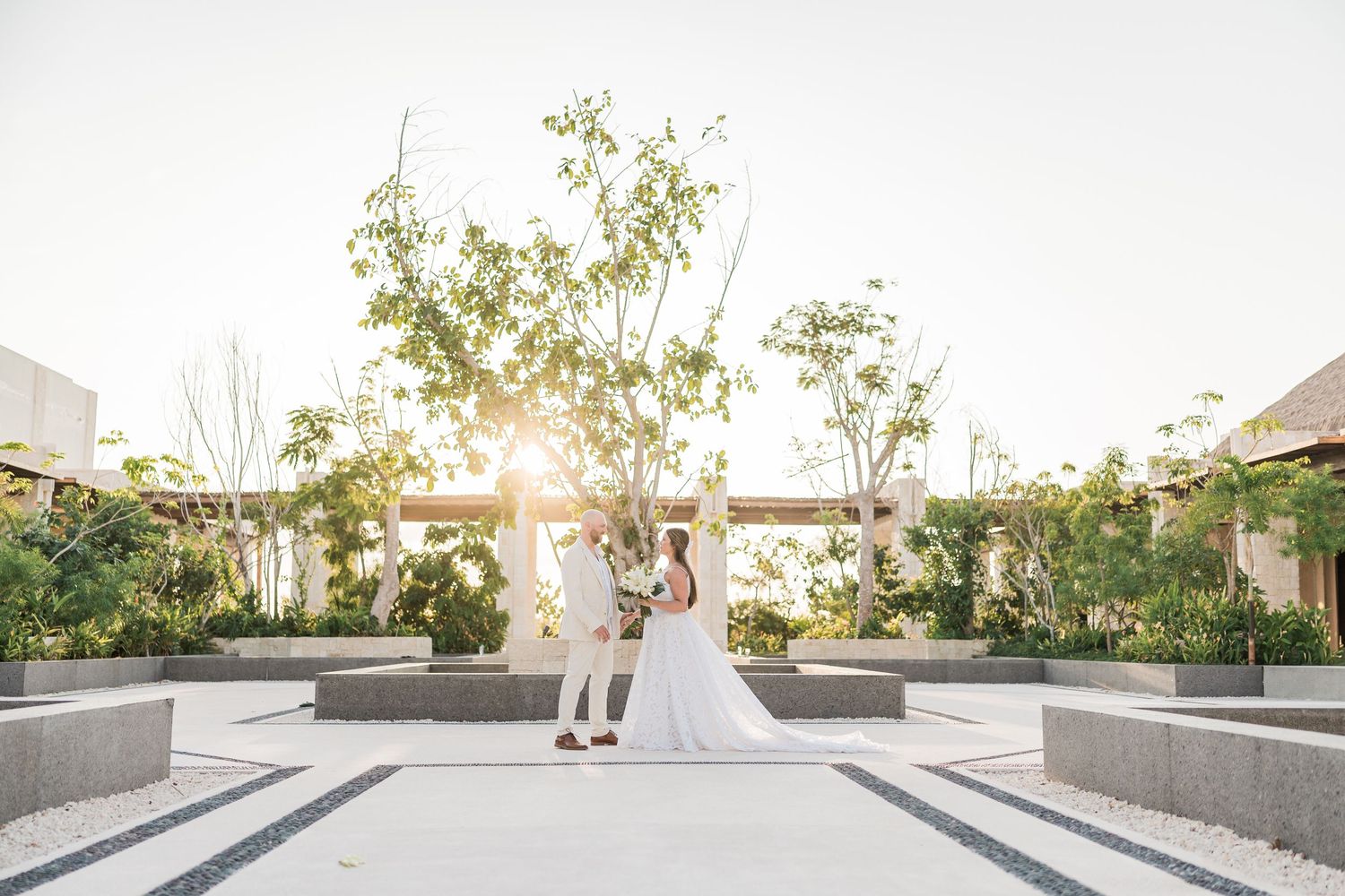 Couple dancing in elegant outdoor wedding venue with lush greenery and golden sunset light.