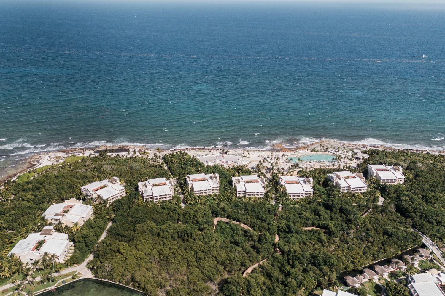 Aerial view of a beachfront resort surrounded by lush tropical trees along a stunning blue Caribbean coastline.