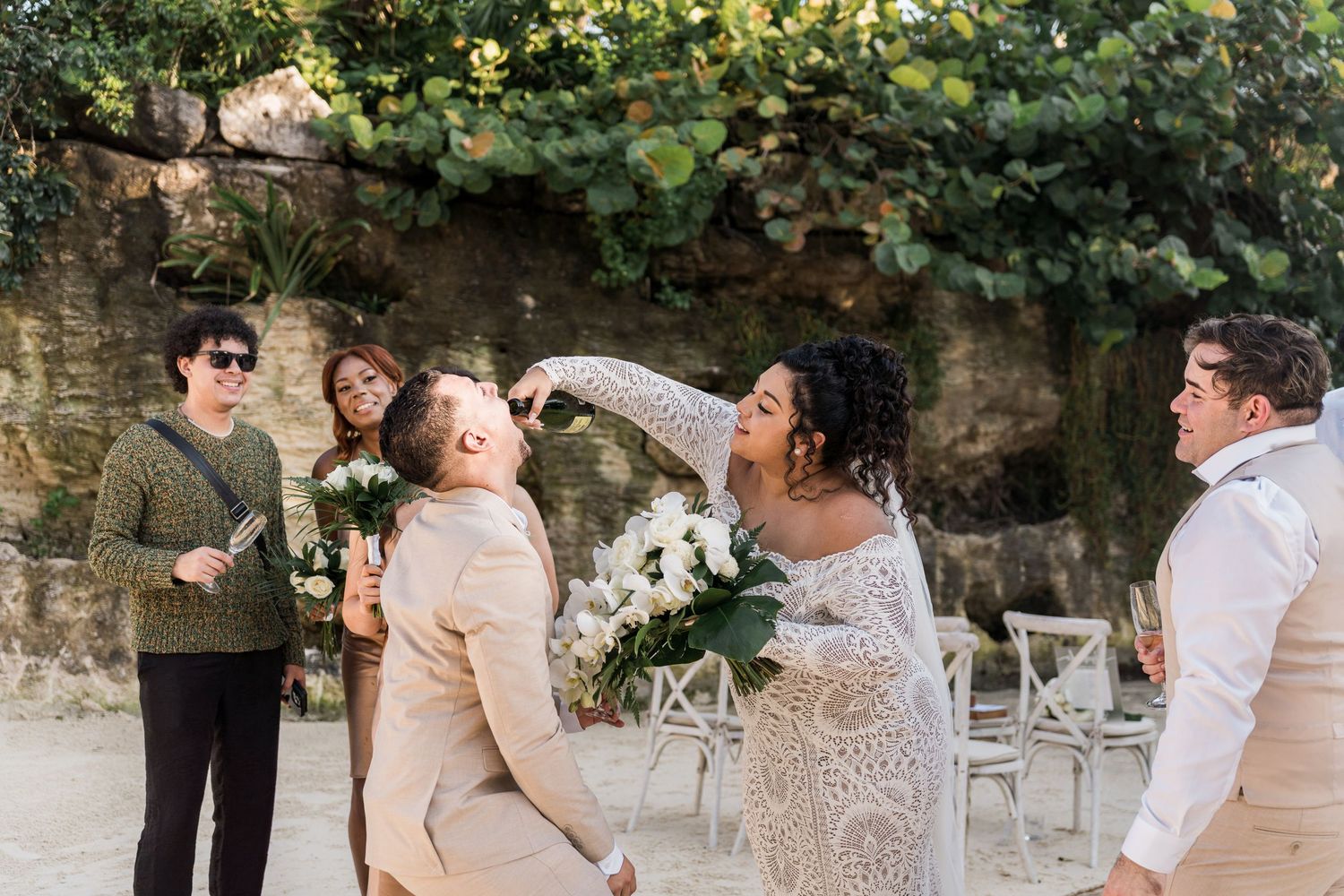 Xcaret Arte Wedding - Bride playfully smashes cake on groom's face at outdoor wedding ceremony while guests laugh and celebrate.