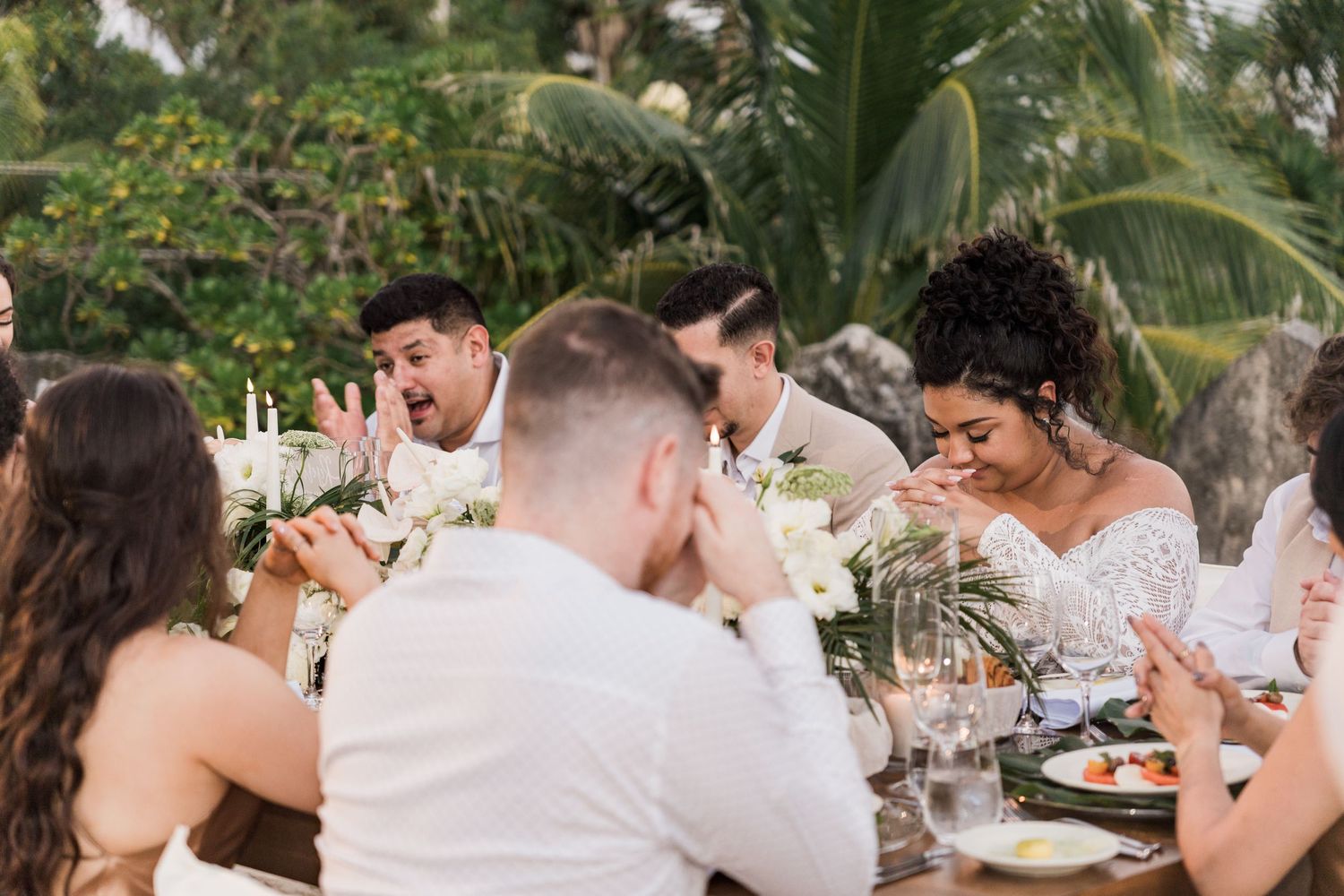 Xcaret Arte Wedding guests laughing and celebrating together at an outdoor tropical reception dinner table with floral centerpieces.