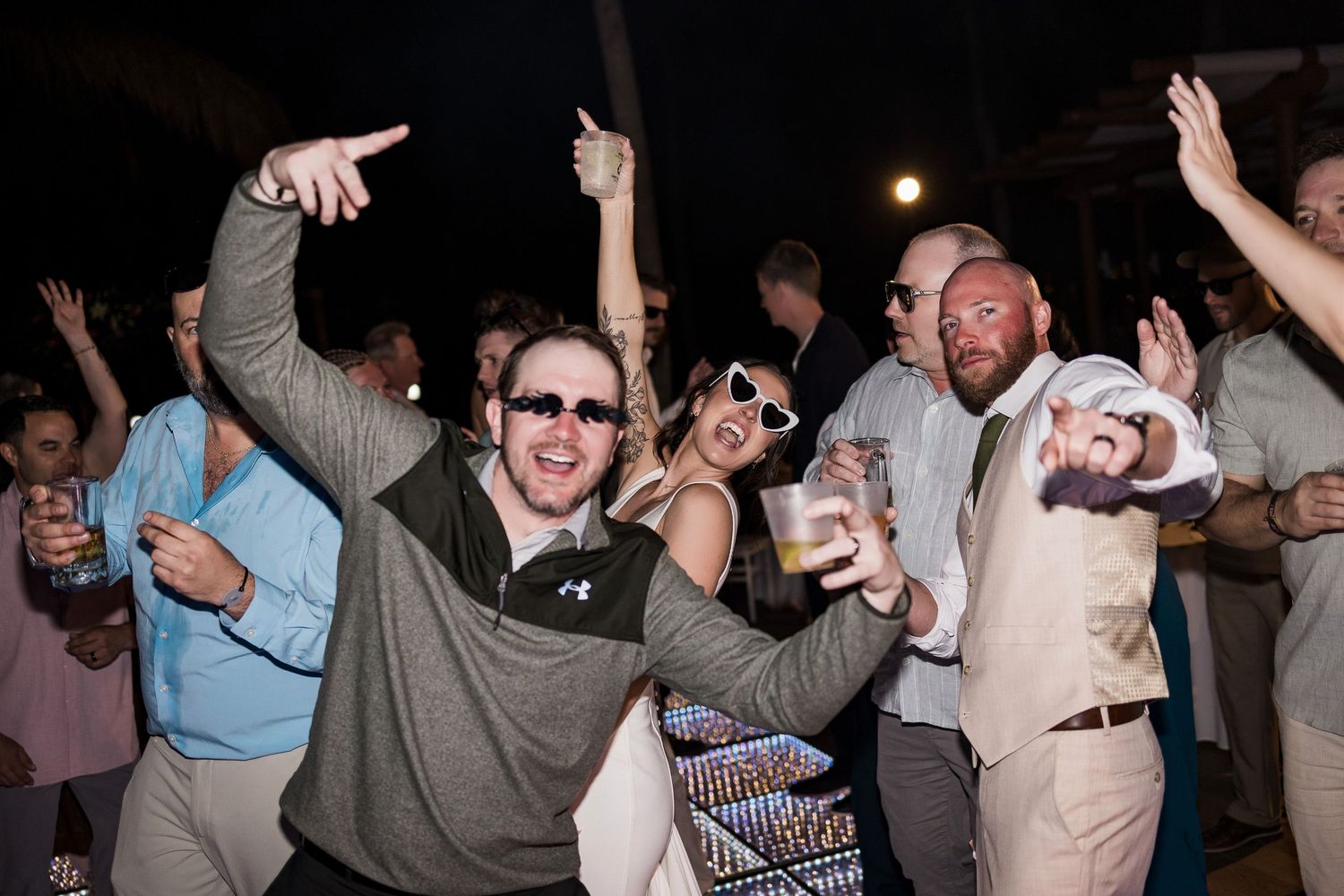 Excited wedding guests dancing and celebrating on outdoor dance floor at night reception.