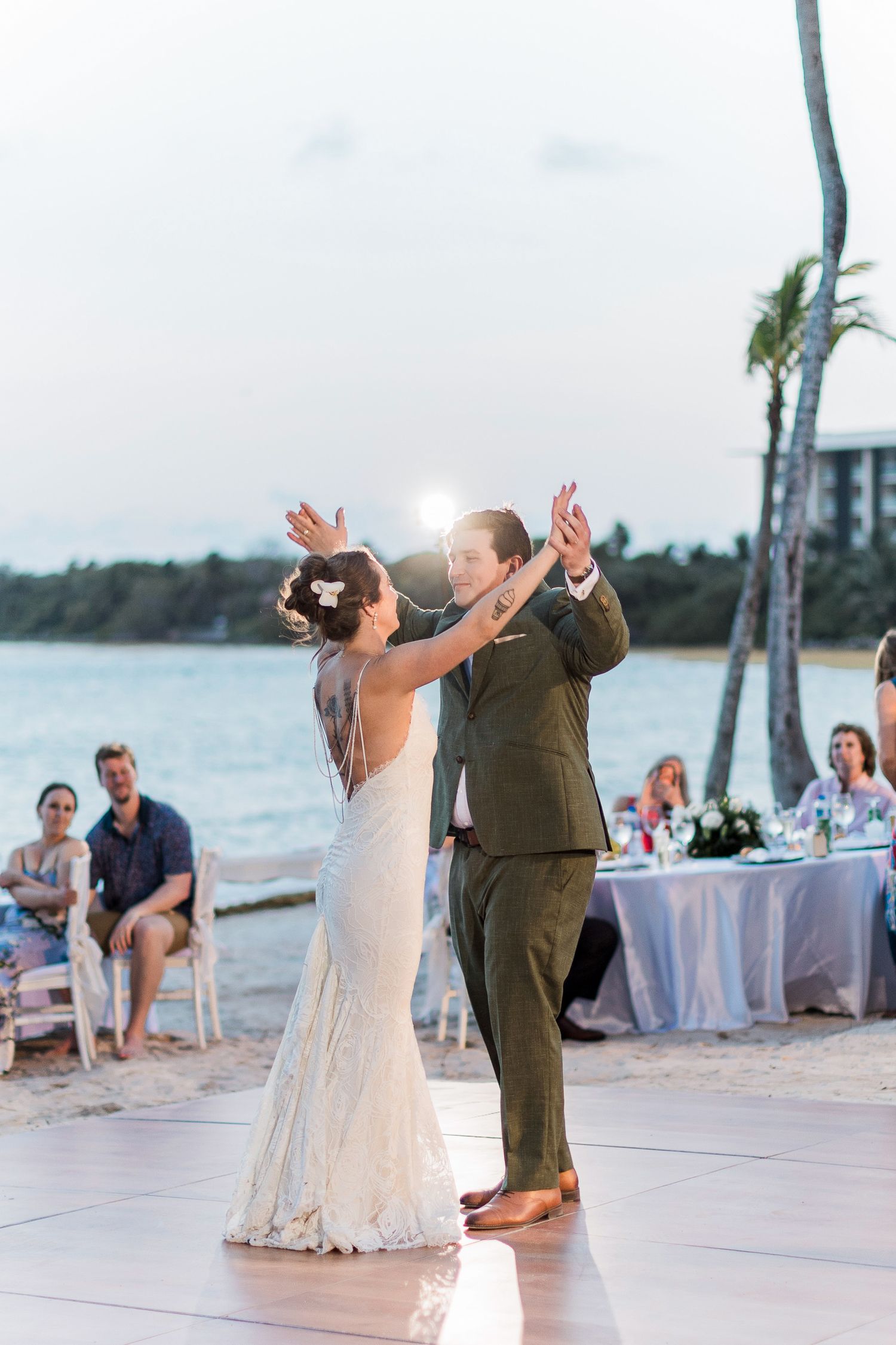 Bride and groom share first dance on beach at sunset wedding reception with ocean backdrop.