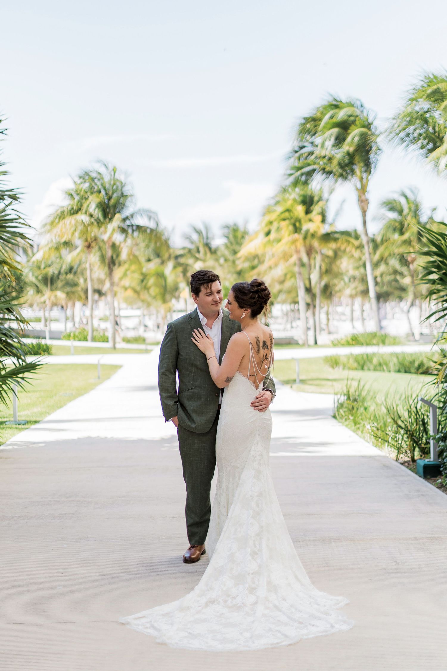 Bride and groom share a romantic moment on a palm-lined path at a tropical wedding venue.