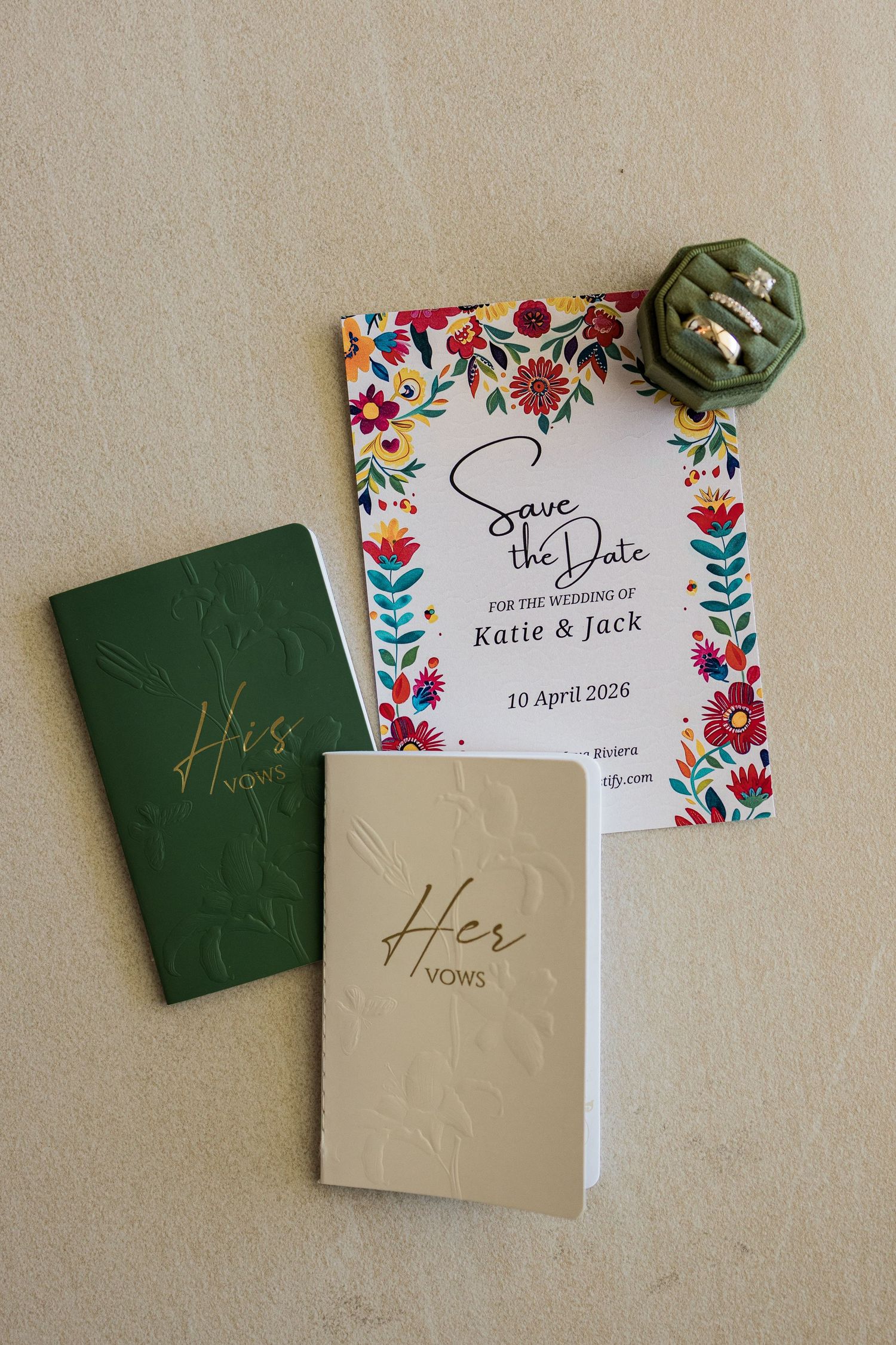 Wedding flat lay with His and Her vows books, floral Save the Date card for Katie & Jack, and green ring box.
