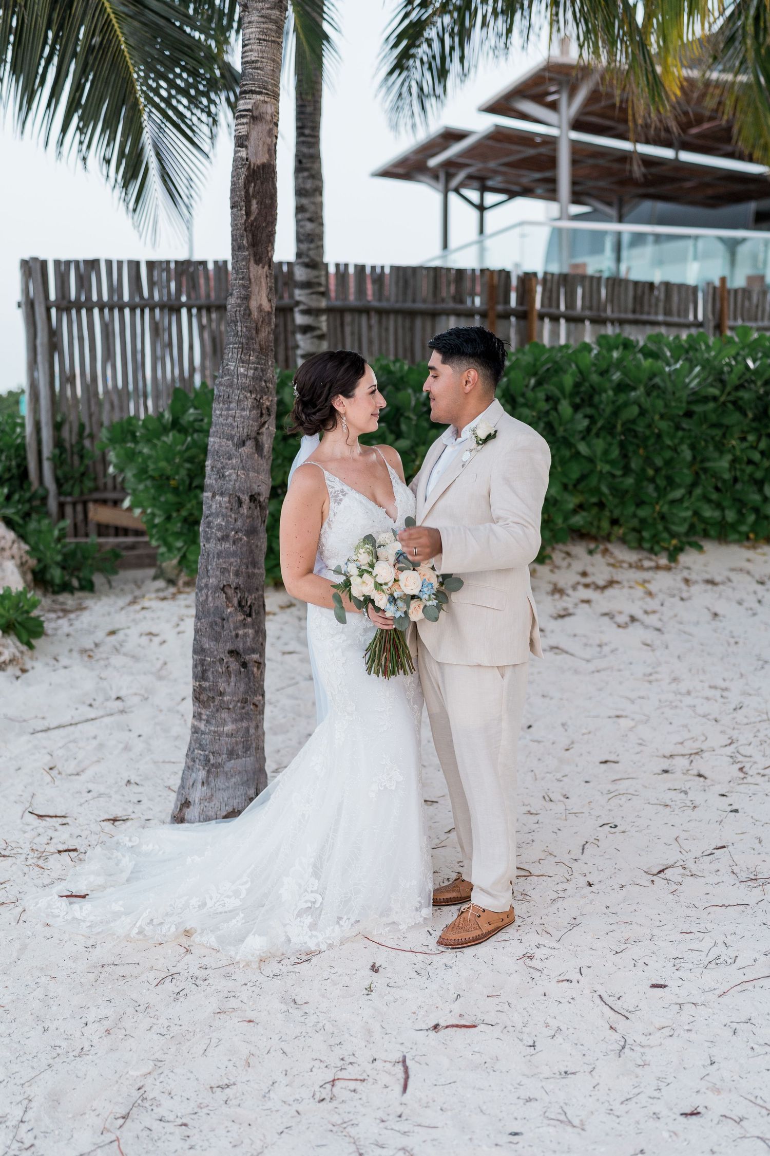 Bride and groom share a romantic moment under palm trees on a white sand beach at their destination wedding.