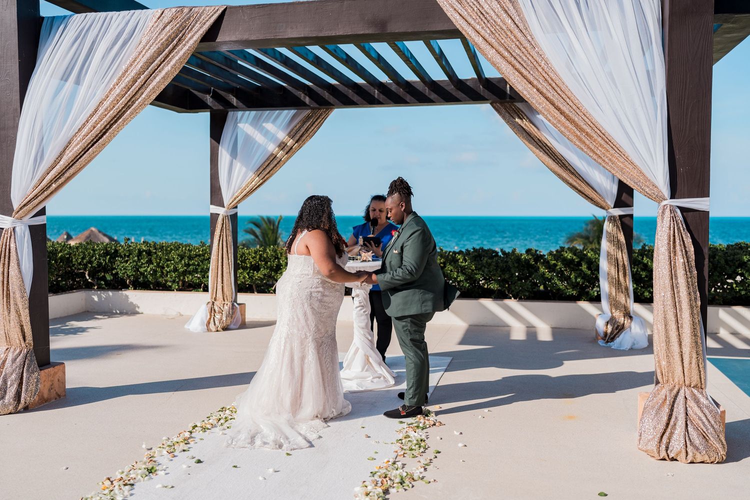 Couple exchanging vows under a draped pergola with ocean views at a destination wedding.