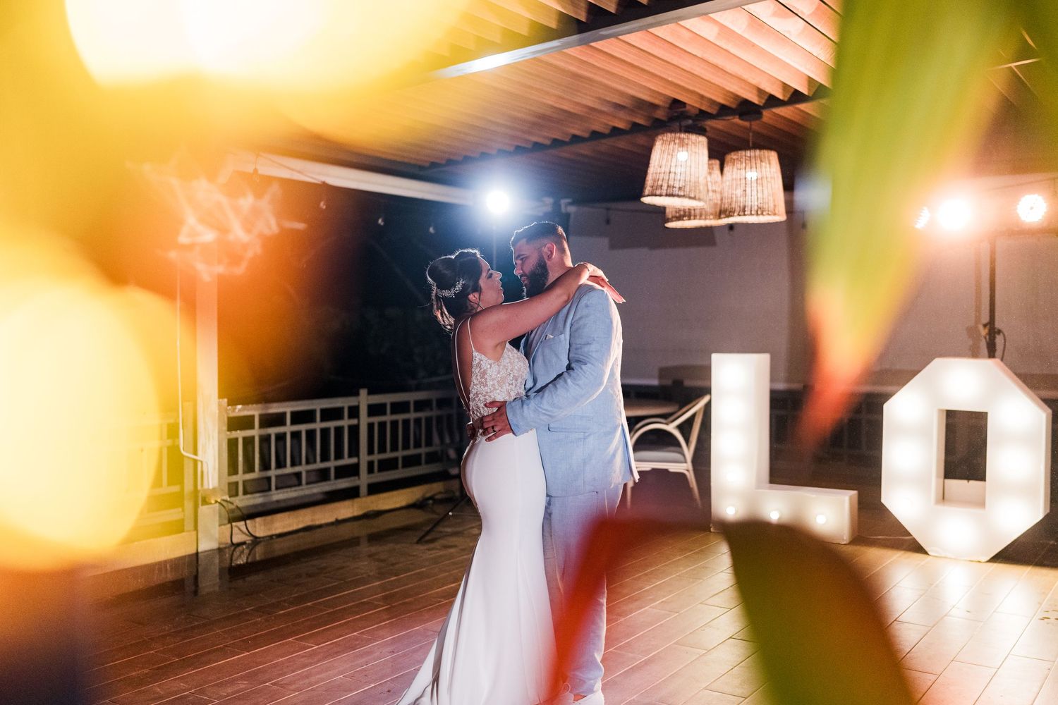 Bride and groom embrace during romantic first dance with glowing LOVE letters at outdoor wedding reception.