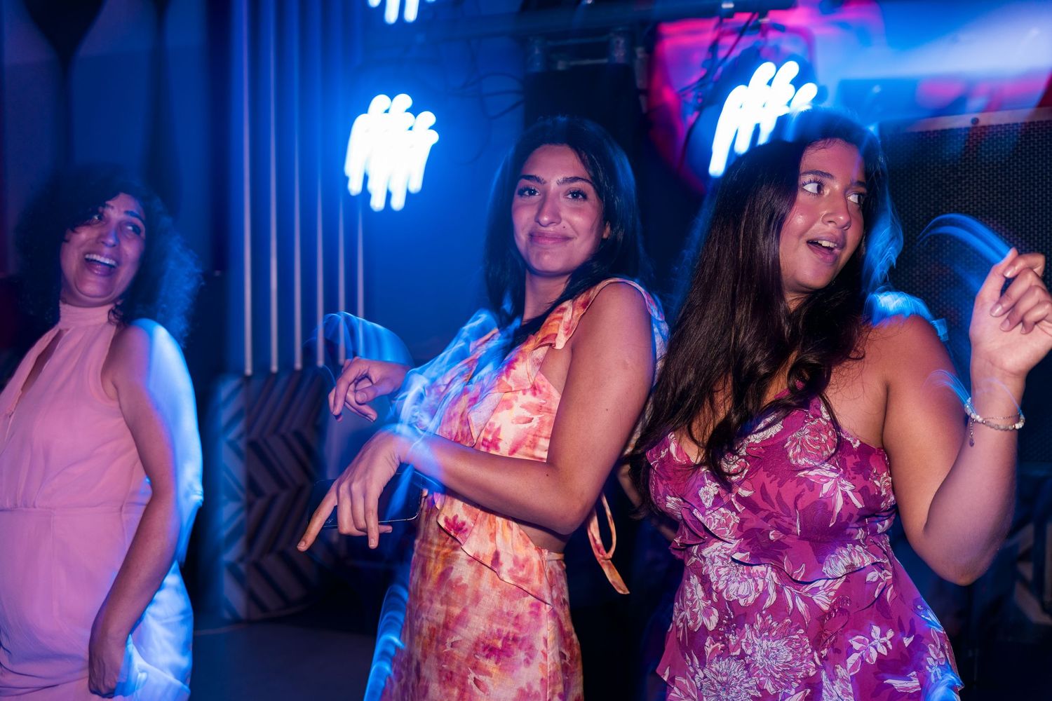 Three women dancing joyfully at a nightclub with blue neon lights.