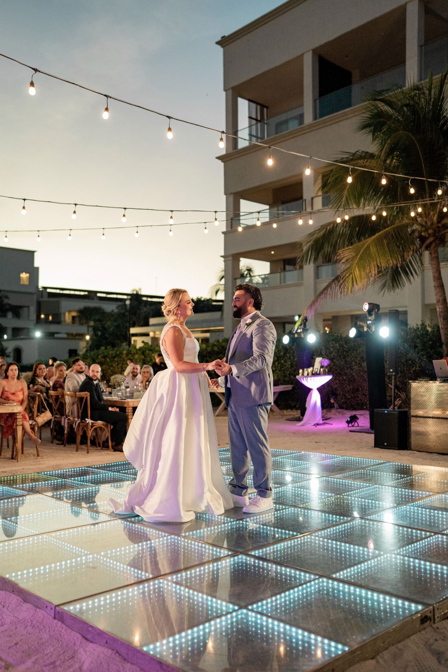 Bride and groom share first dance on illuminated LED dance floor at outdoor wedding reception.