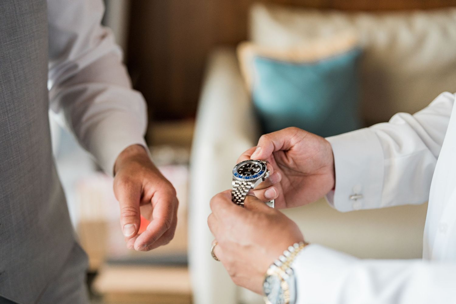 Man in white dress shirt adjusting a luxury Rolex watch on his wrist during a formal event.