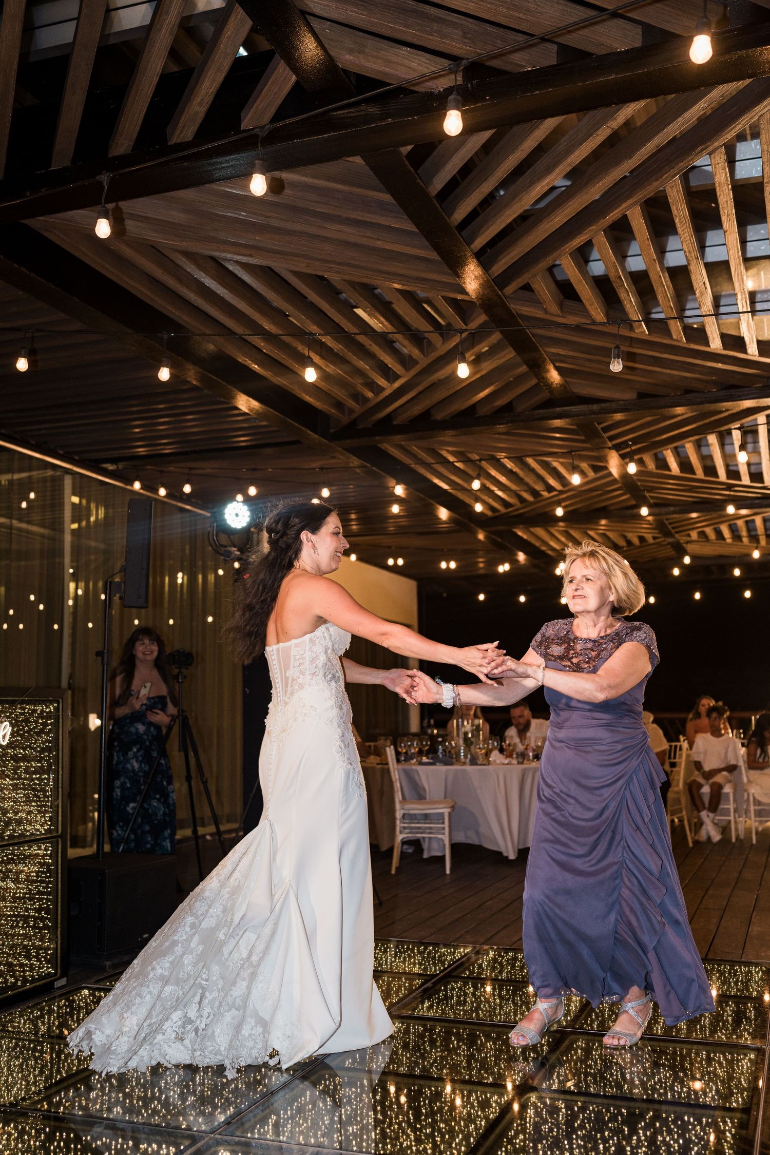 Bride and mother dancing together on a sparkling dance floor under warm string lights at an elegant wedding reception.