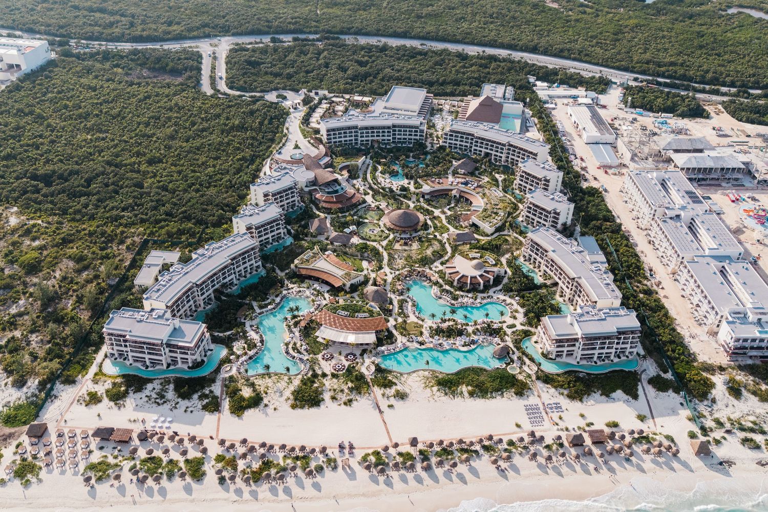 Aerial view of a luxury beachfront resort with pools, lush gardens, and white sand beach in a tropical destination.