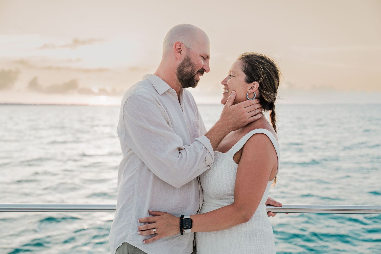 Romantic couple sharing a tender moment on a boat deck with ocean sunset backdrop.