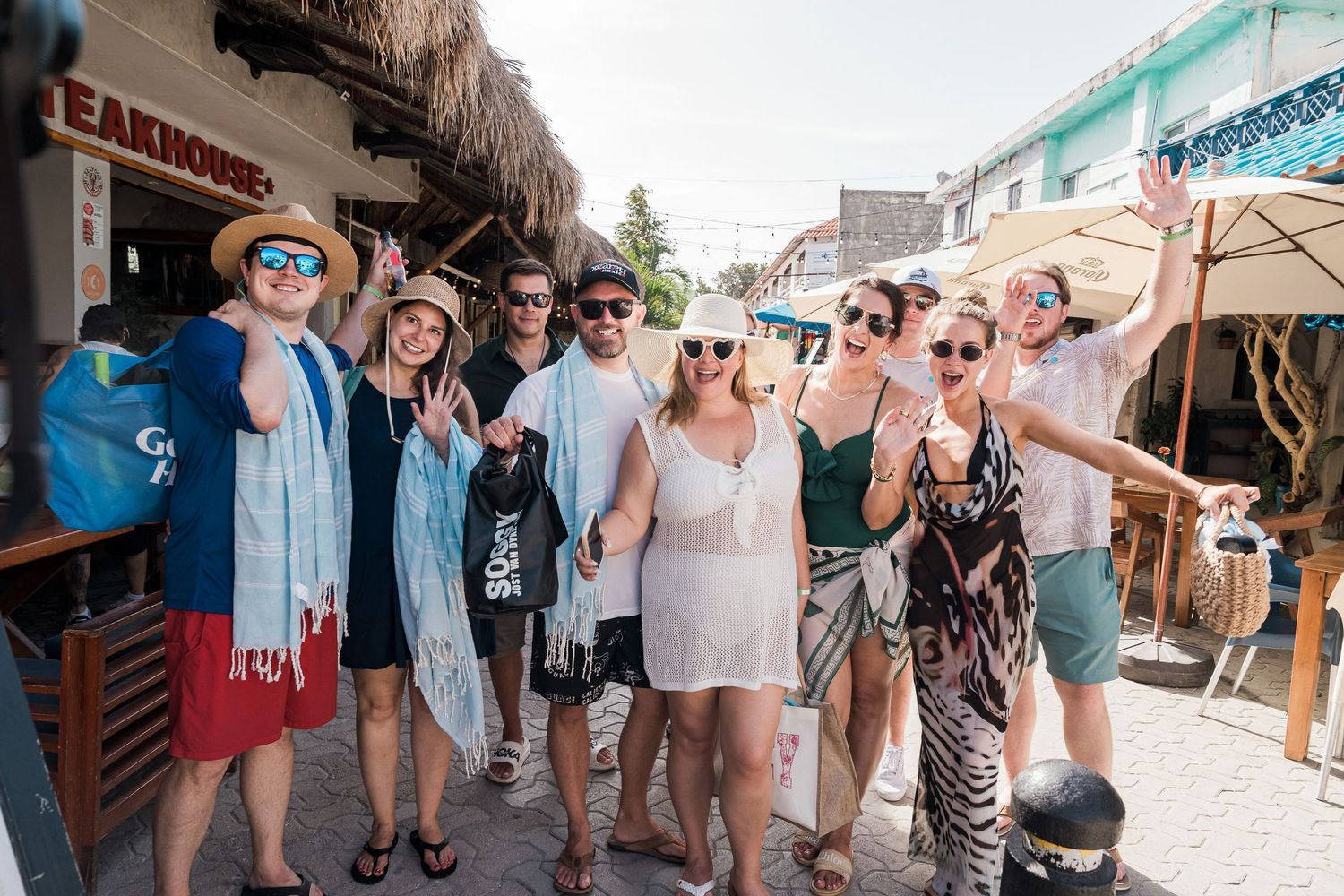 Riviera Maya Multi Day wedding - Group of tourists posing together on a sunny street near a steakhouse in a tropical beach town.