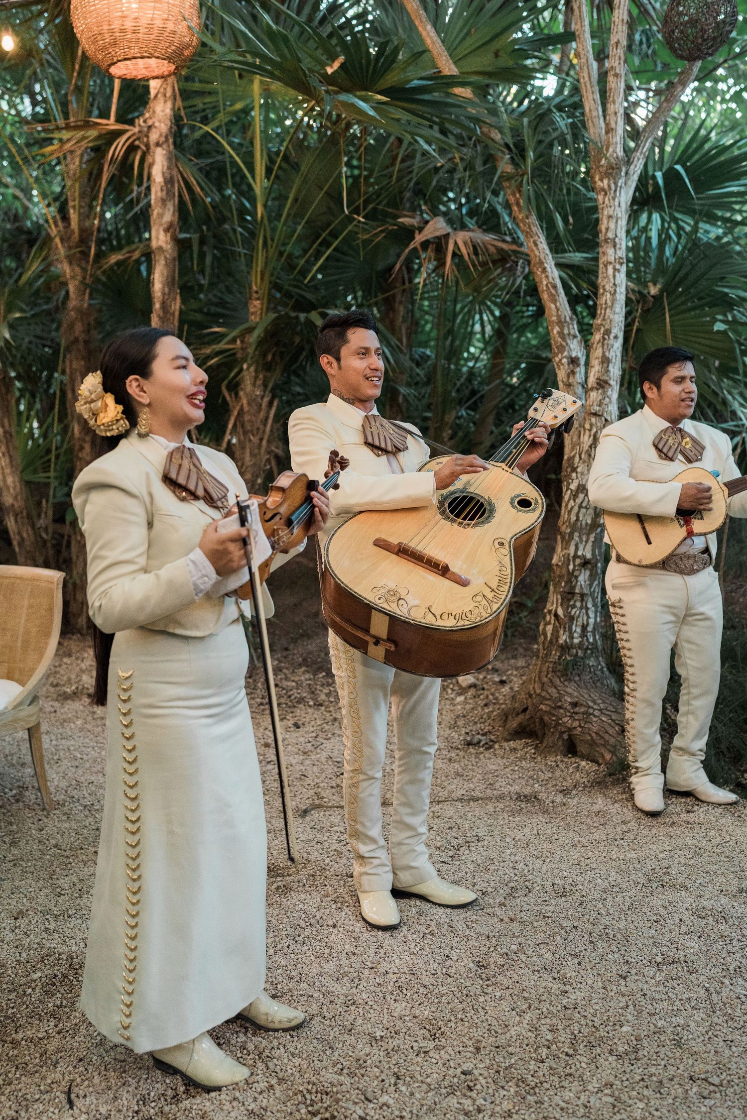 Secrets Akumal Wedding - Mariachi band in white traditional suits performing outdoors among tropical trees at a festive event.