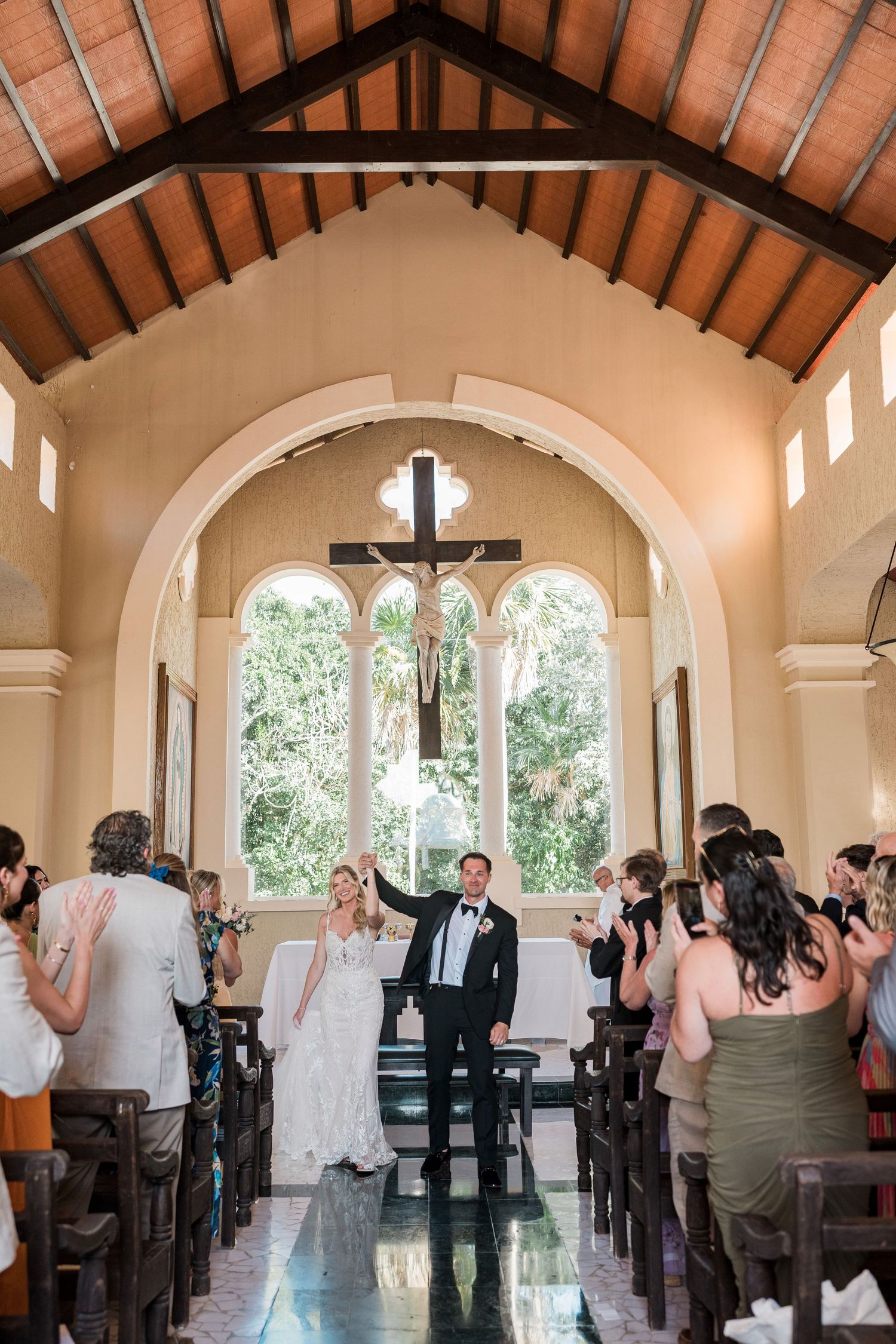 Bride and groom celebrate at the altar of a charming chapel with wooden ceilings and arched windows.