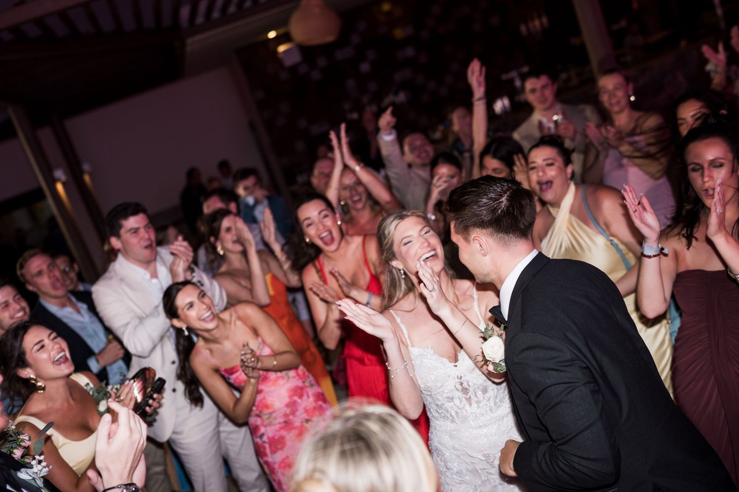 Joyful wedding reception dance floor with bride in white dress celebrating with guests, arms raised in festive atmosphere.