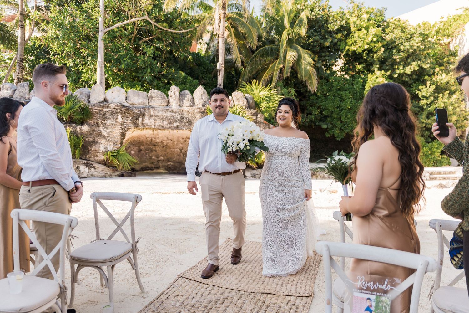 Xcaret Arte Wedding - Bride and groom celebrate at outdoor wedding ceremony surrounded by guests and lush tropical greenery.