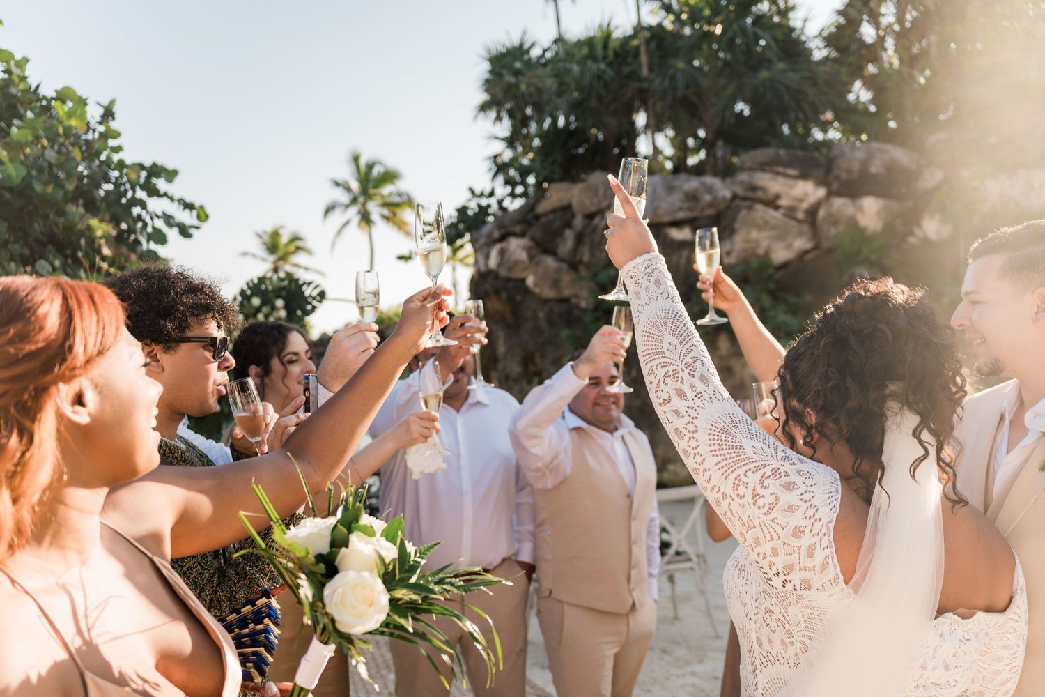 Xcaret Arte Wedding - Bride and groom toasting champagne with guests at a tropical beach wedding celebration.