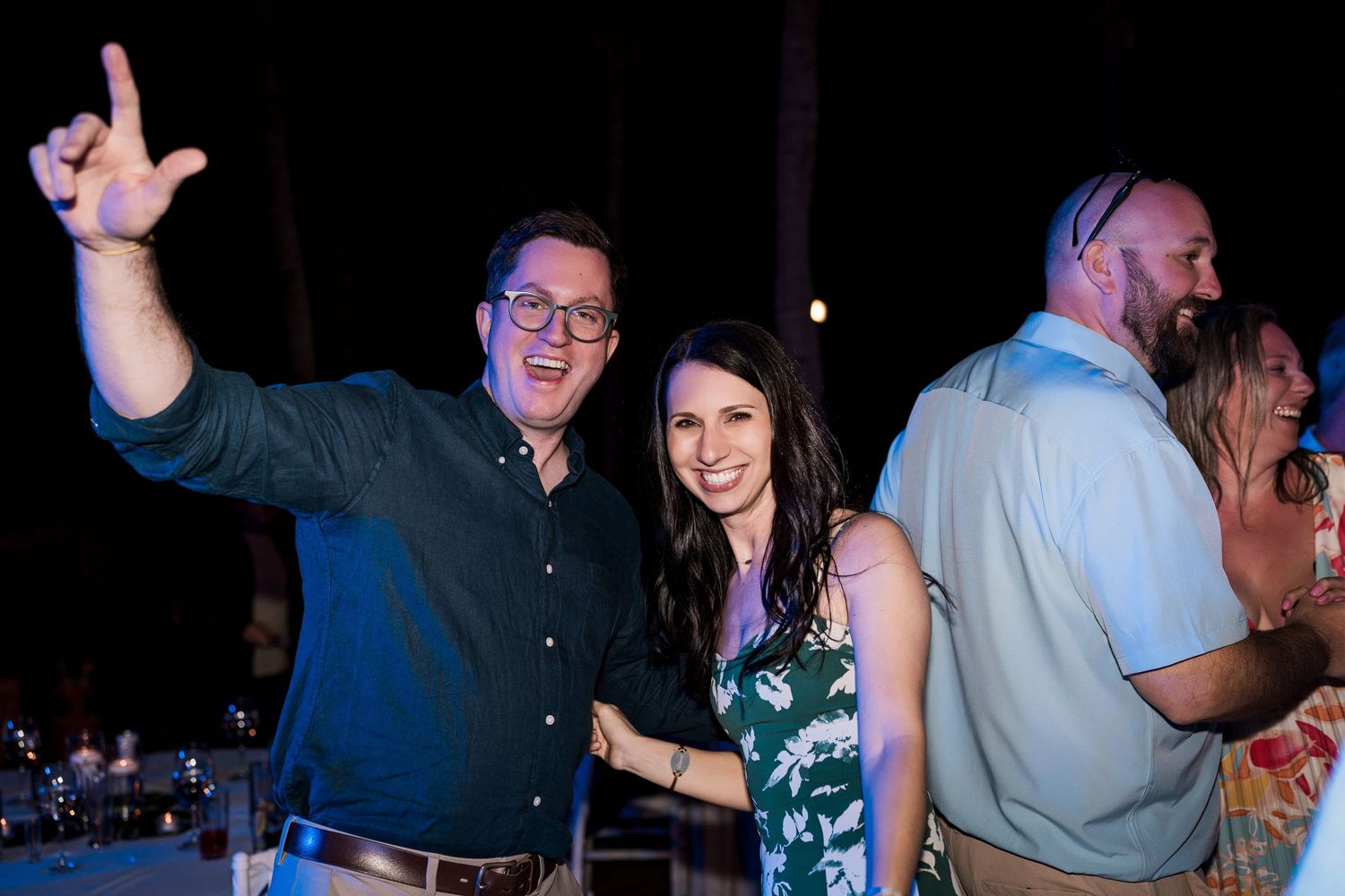 Two people smiling and posing at an outdoor evening party, man pointing up with finger gun gesture.