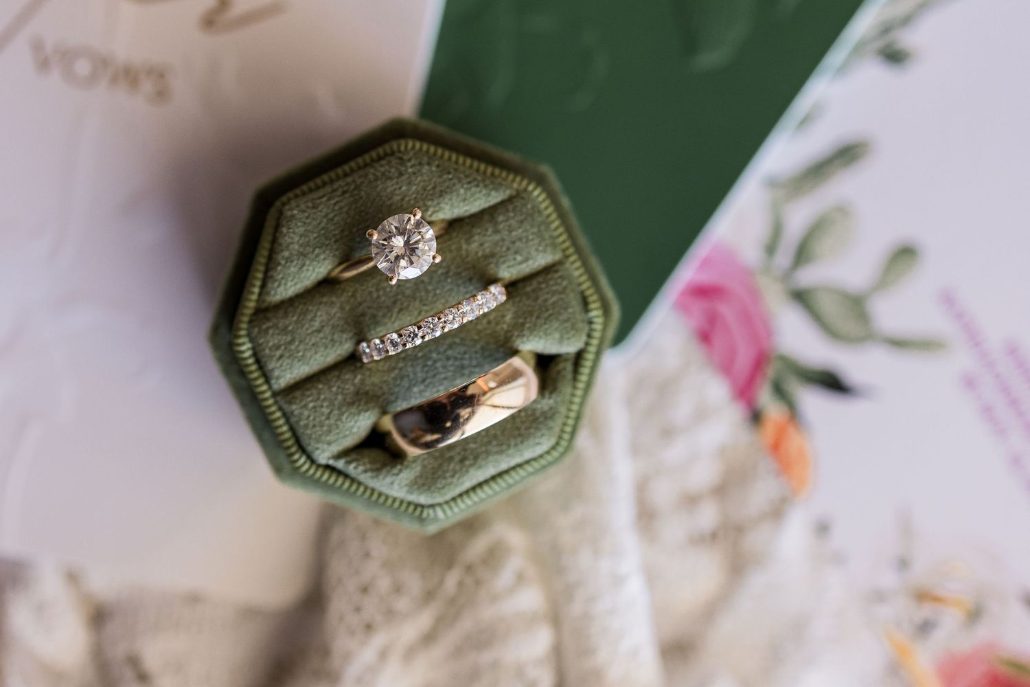 Three wedding rings displayed in a green velvet octagonal ring box, featuring a diamond solitaire engagement ring.