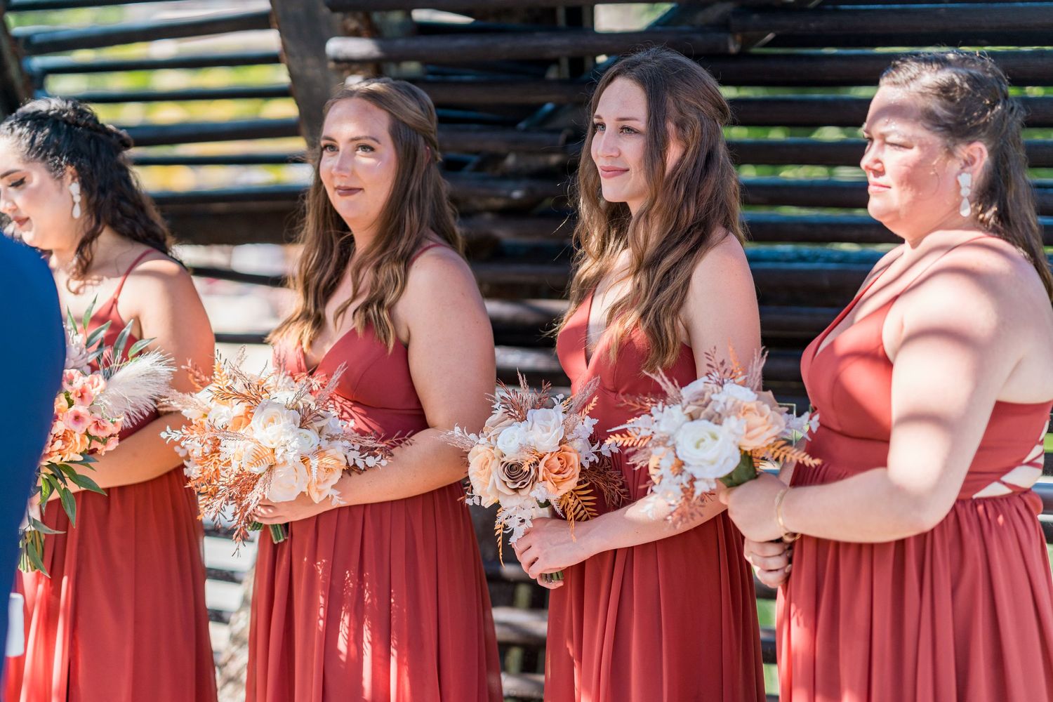 Four bridesmaids in red dresses holding bouquets of peach and white flowers at wedding.