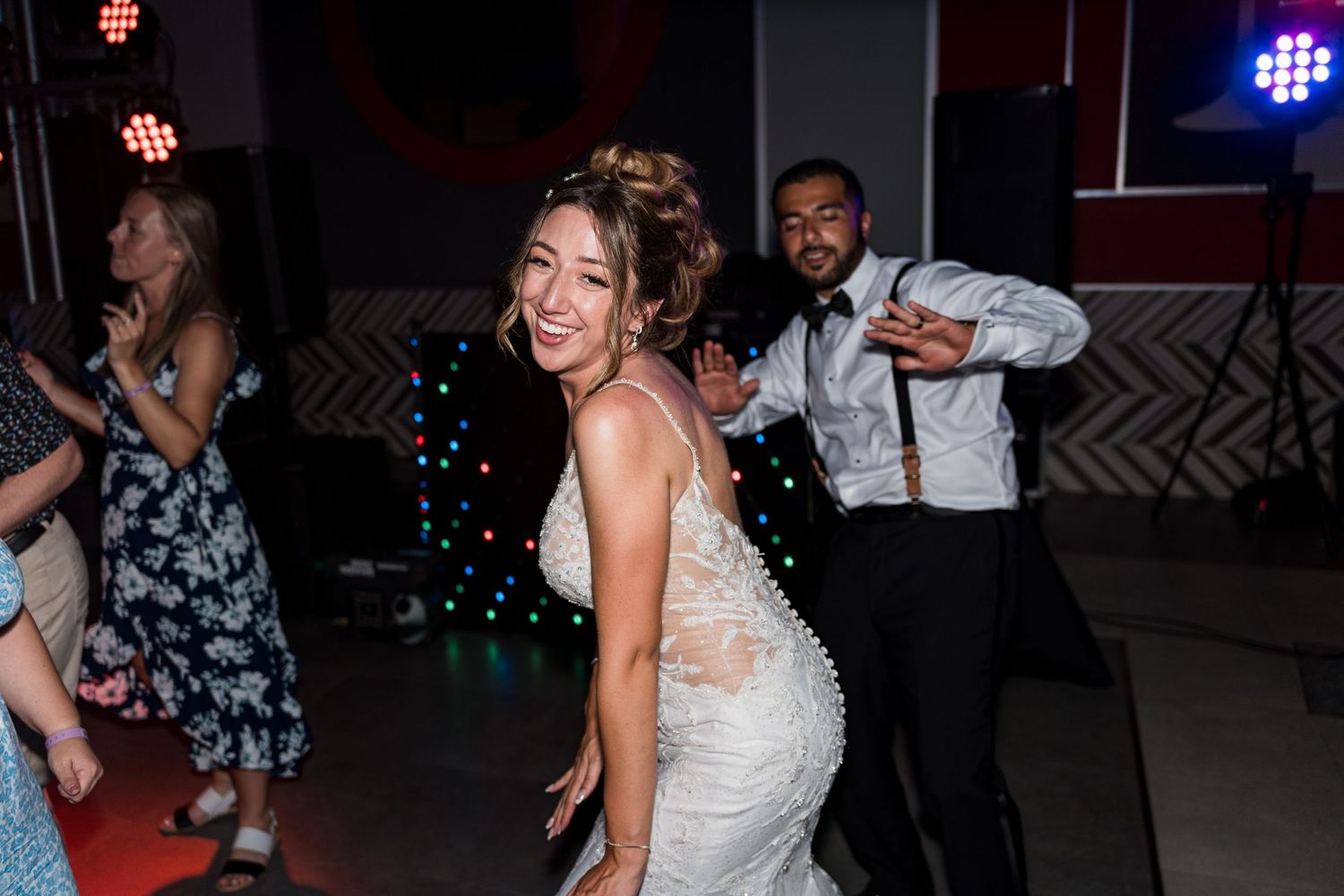 Bride in lace wedding gown dances joyfully with guests at energetic wedding reception party.