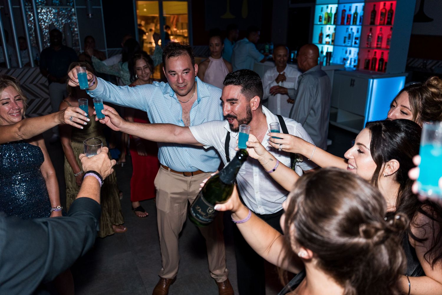 Groom pouring champagne for guests during lively outdoor wedding reception celebration.