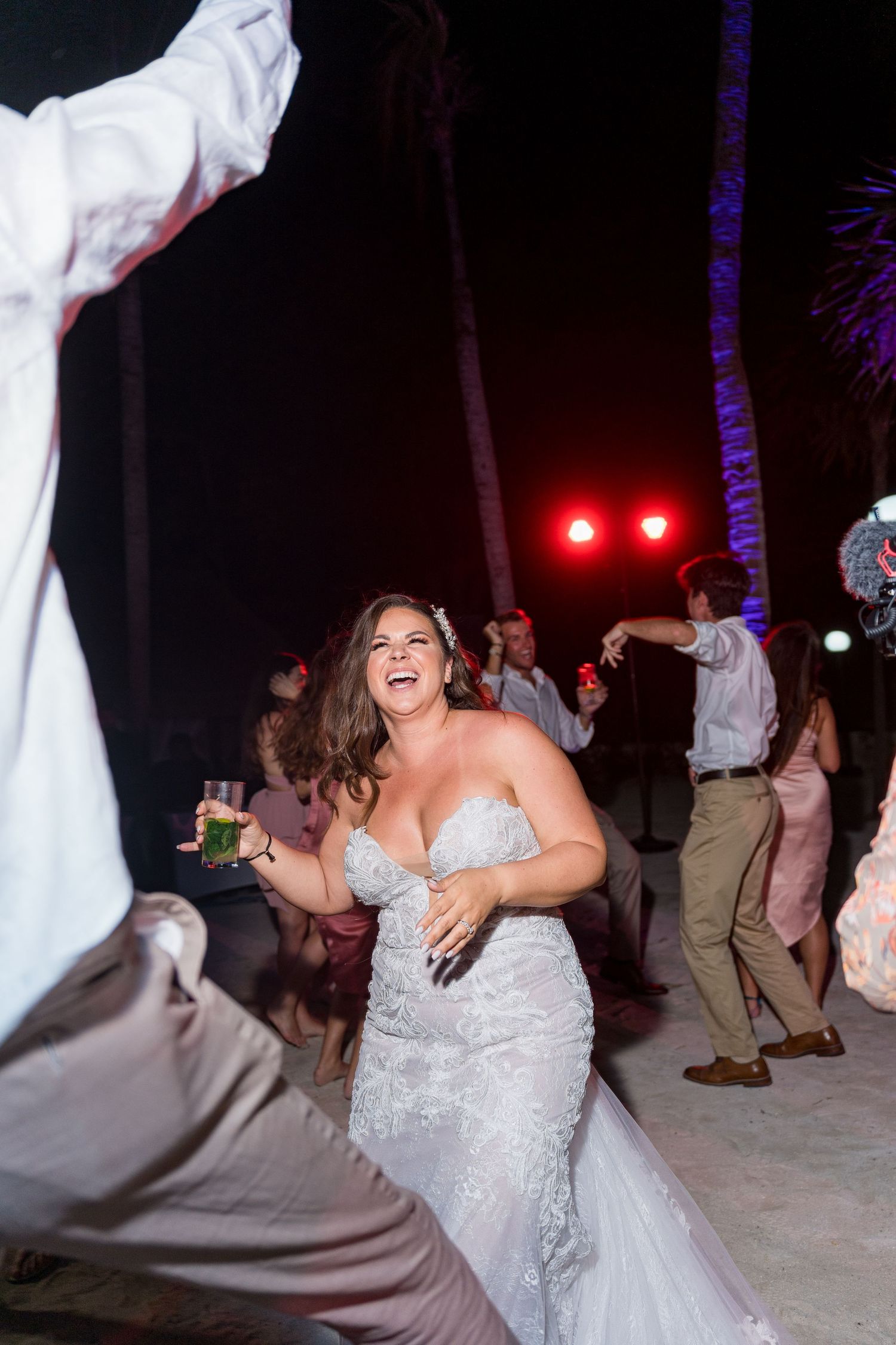 Radiant bride in a fitted lace gown laughs while dancing at an outdoor beach wedding reception.