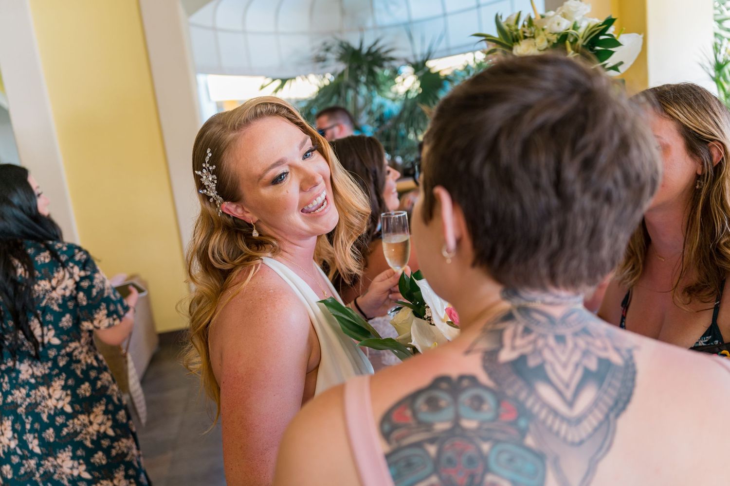 Bride smiling joyfully at a tattooed guest during a tropical wedding reception.