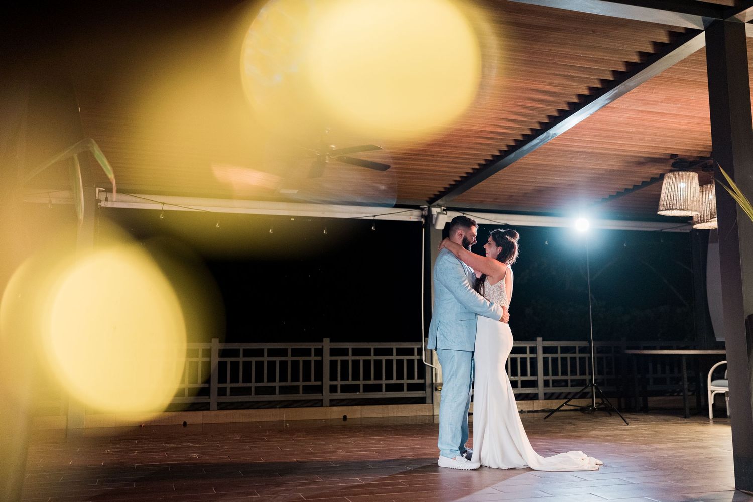 Newlywed couple shares a romantic first dance embrace under outdoor venue lighting at night reception.