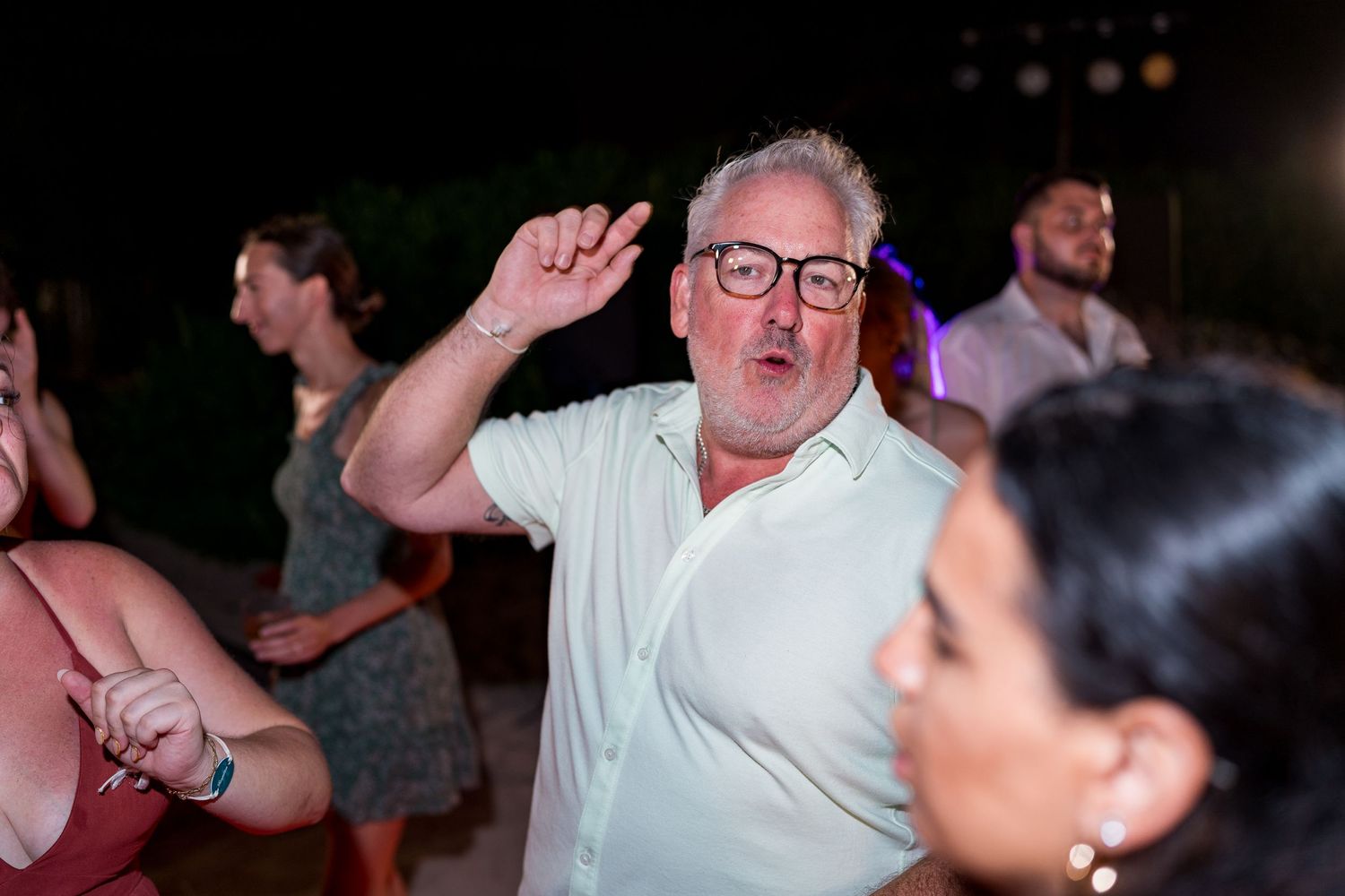 Older man dancing enthusiastically at an outdoor evening wedding reception.