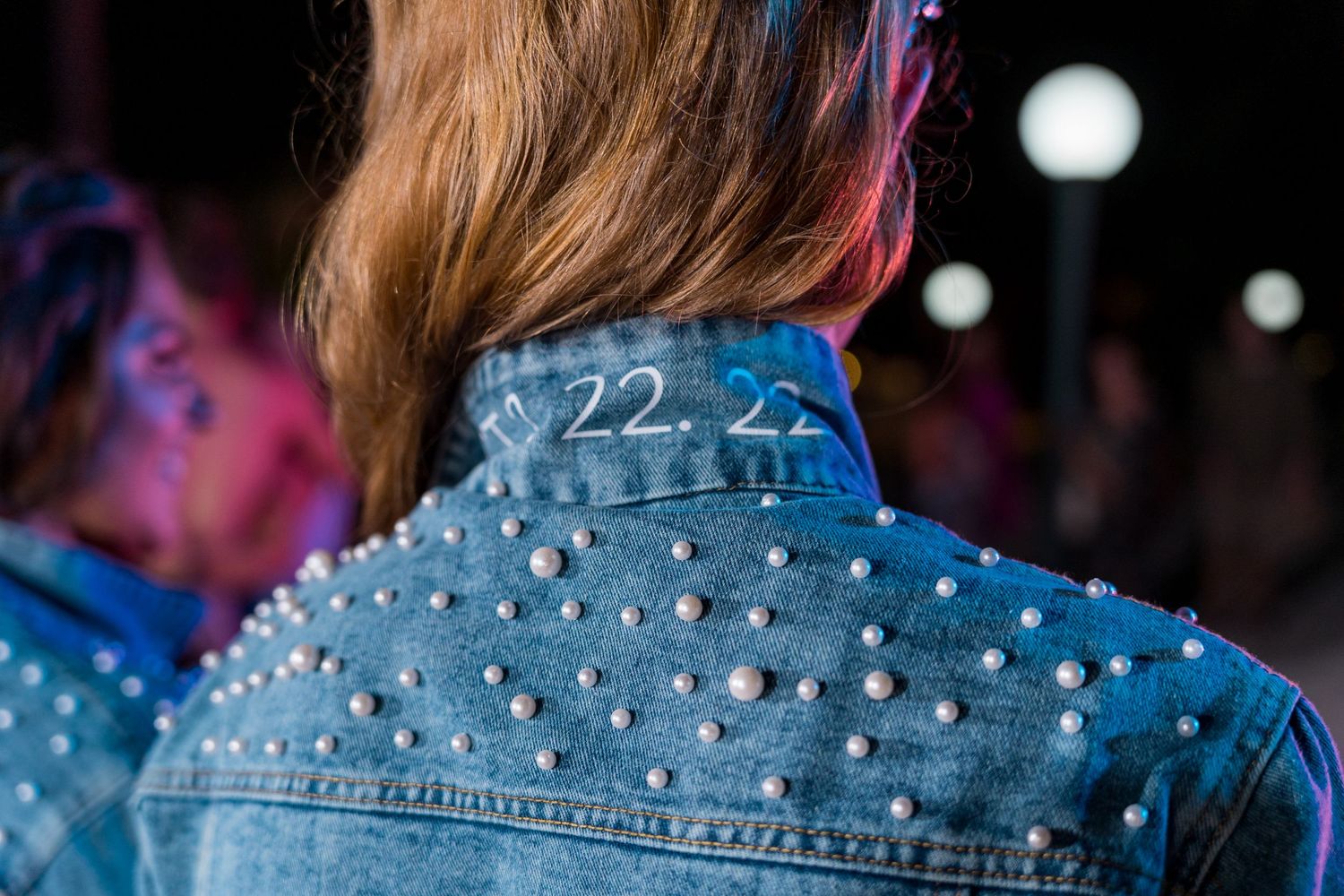 Back view of a pearl-studded denim jacket with '22.22' written on the collar at a wedding reception.