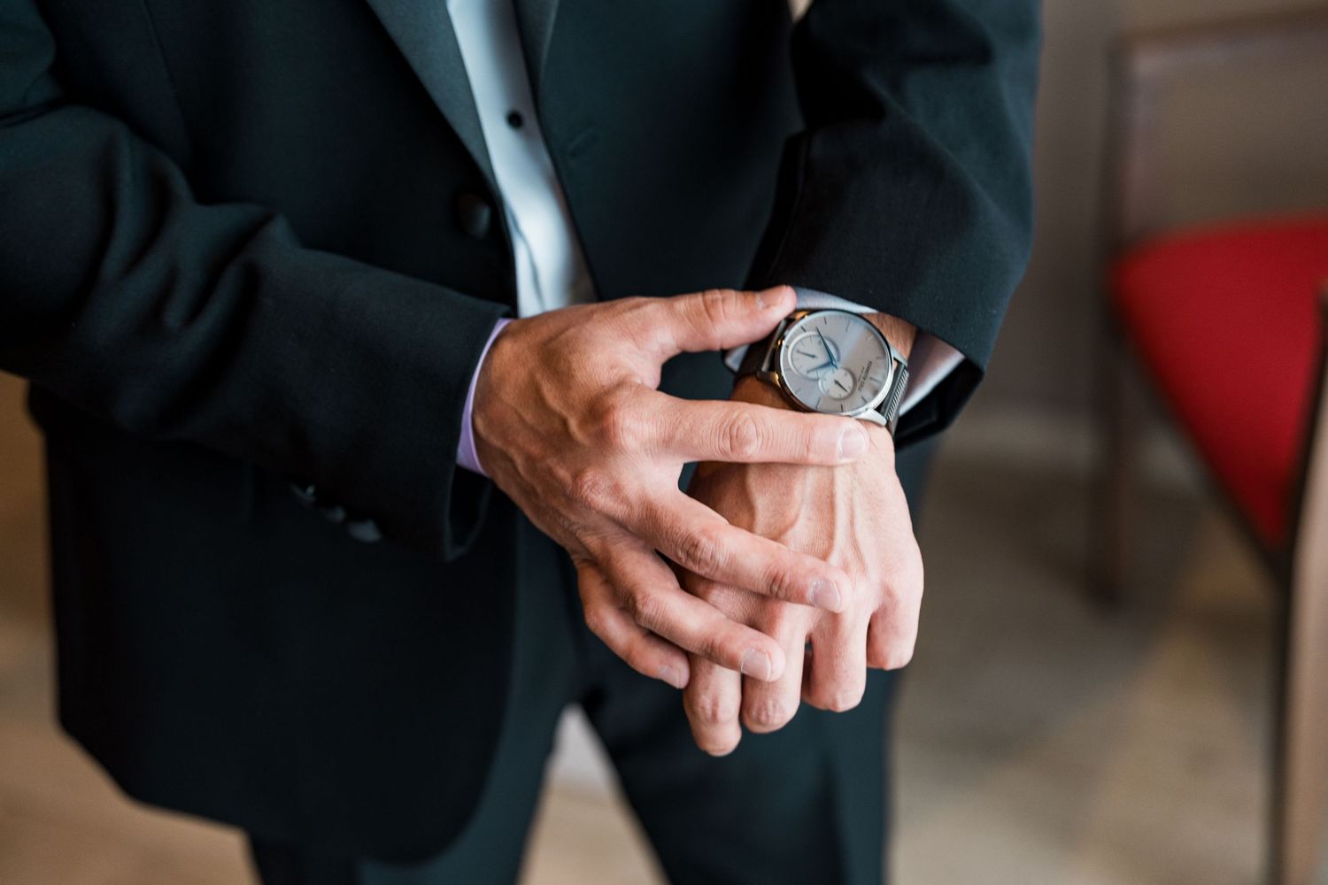 Close-up of groom adjusting elegant silver watch on wrist in black suit.