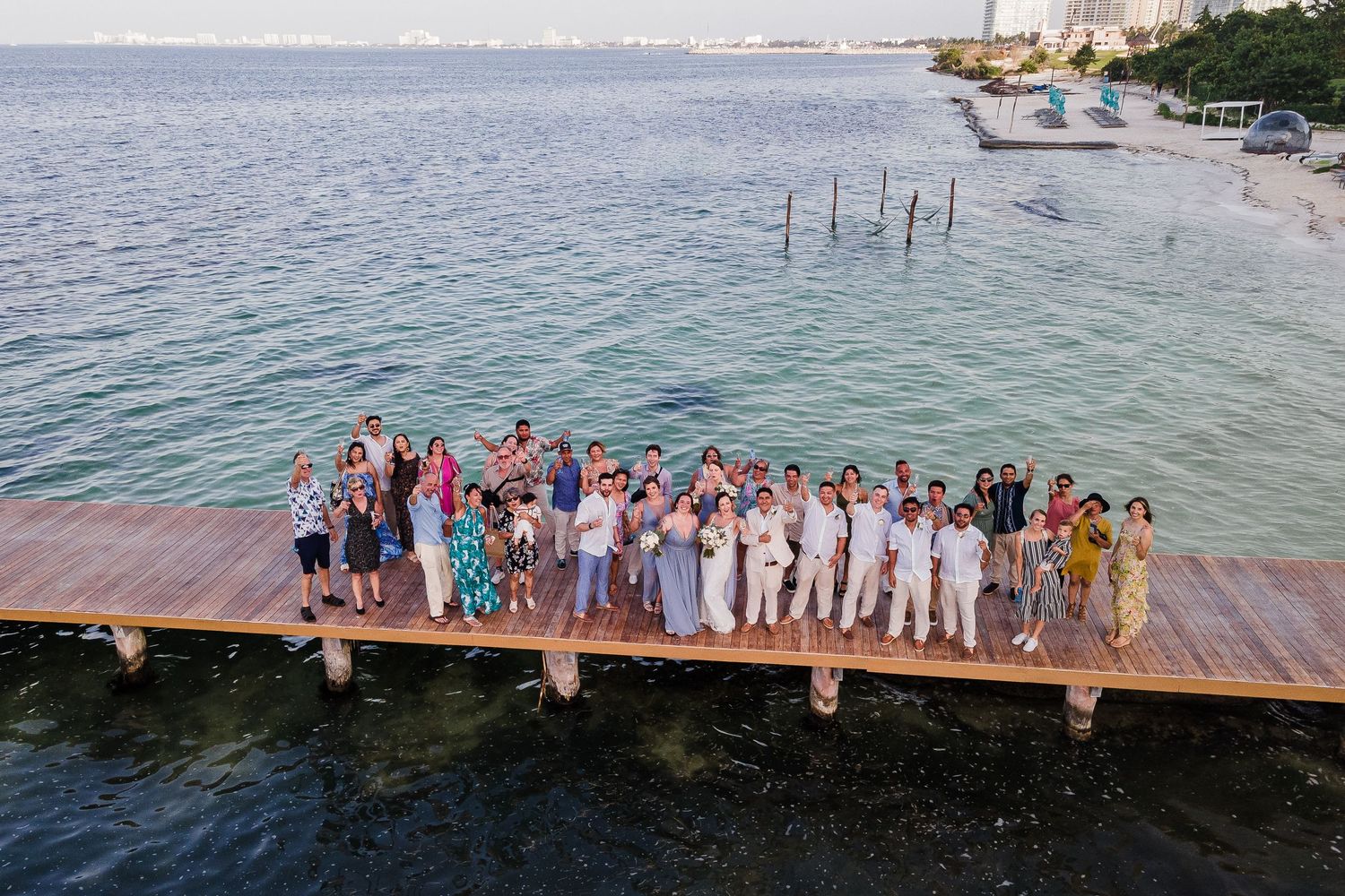 Aerial view of wedding guests posing on a wooden pier surrounded by turquoise Caribbean waters.