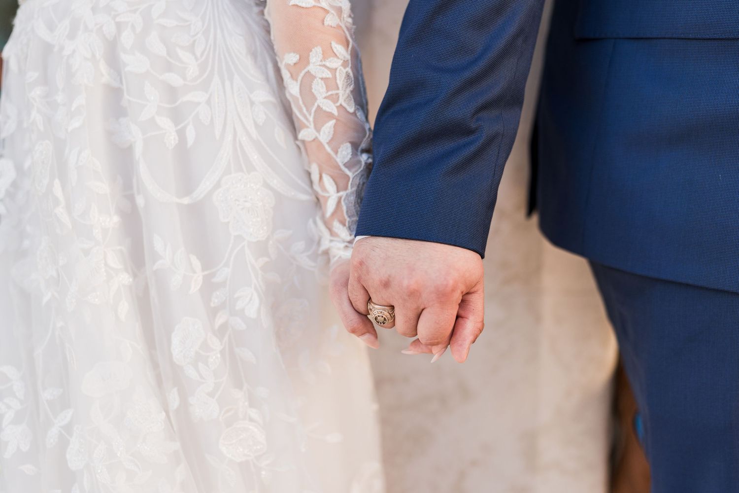 Close-up of bride and groom holding hands showing wedding ring and lace dress sleeve.