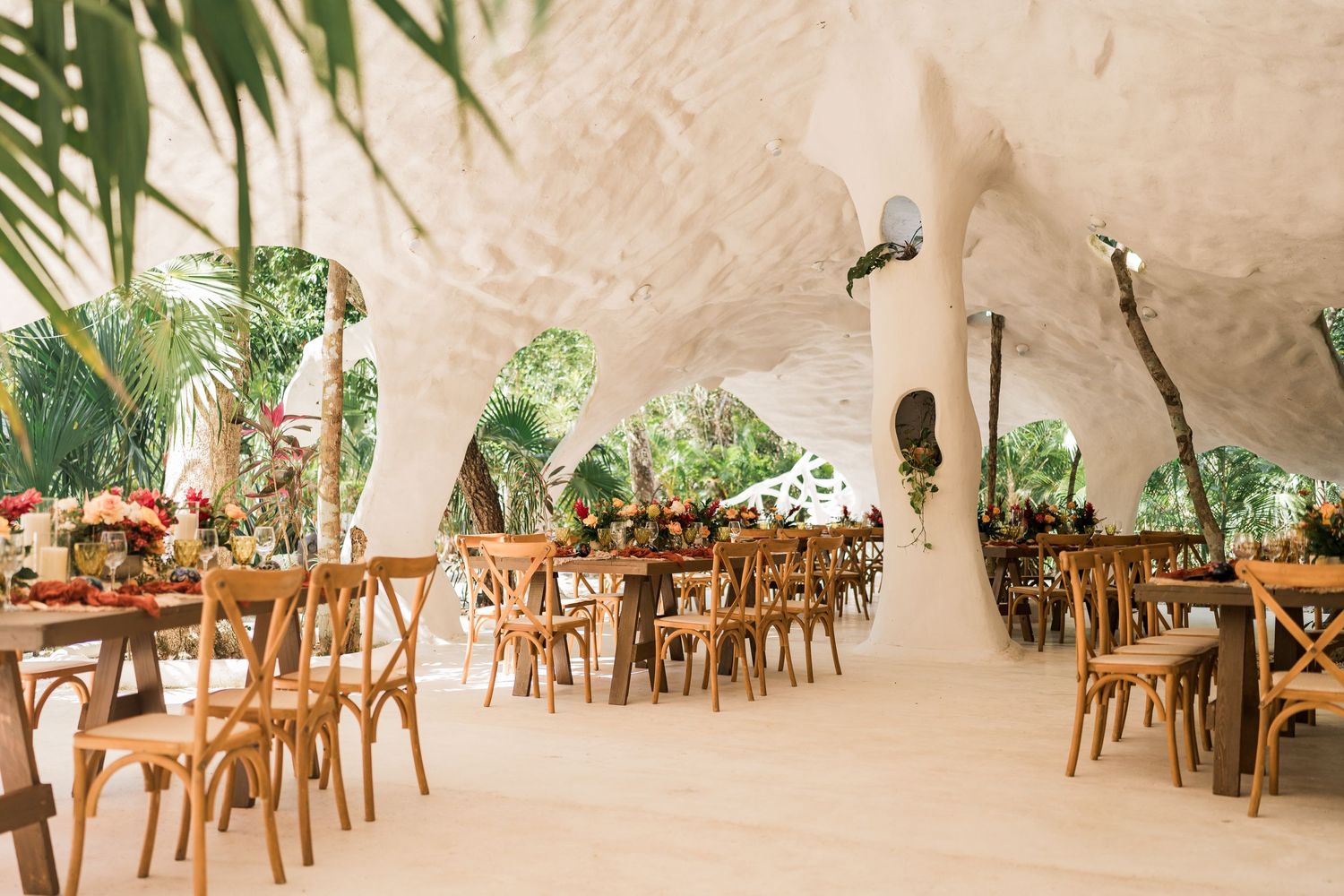 Elegant cave wedding reception venue with wooden cross-back chairs and tropical floral centerpieces.