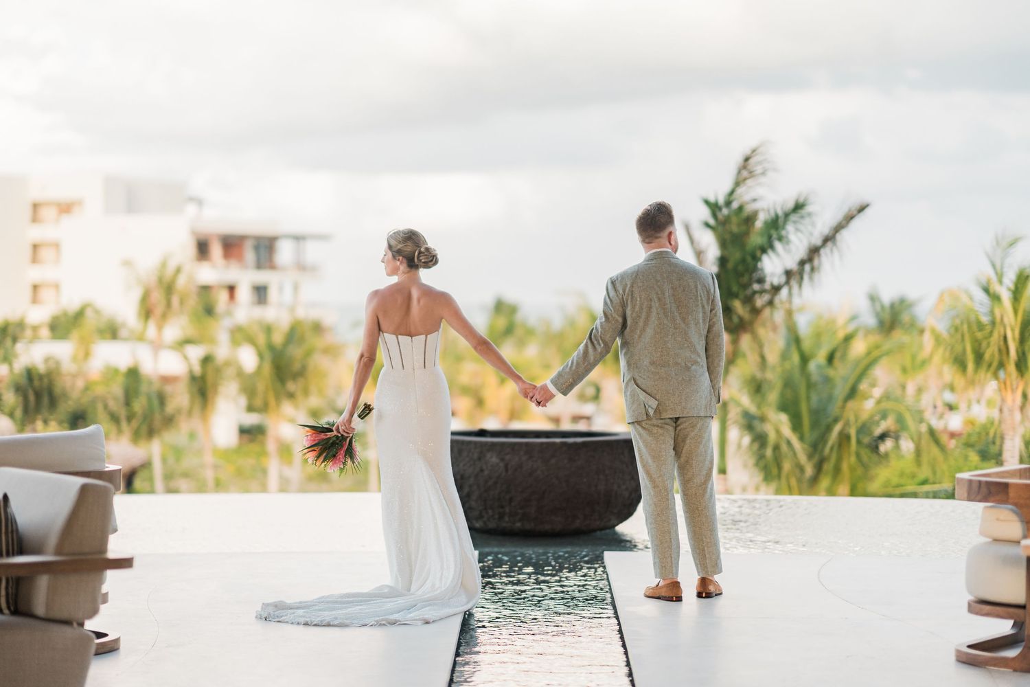 Bride and groom holding hands overlooking tropical resort landscape on their wedding day.