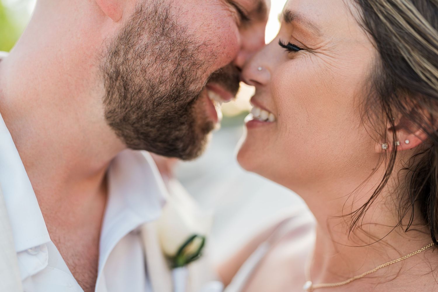 Close-up of smiling bride and groom touching foreheads, groom wearing boutonniere, romantic wedding portrait.