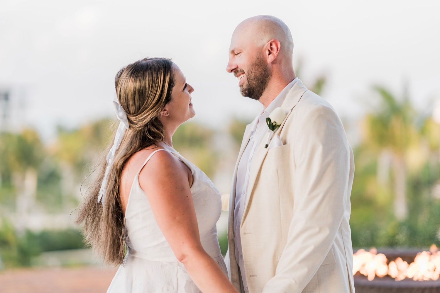 Bride and groom share a romantic moment holding hands at an outdoor wedding ceremony with tropical palms.