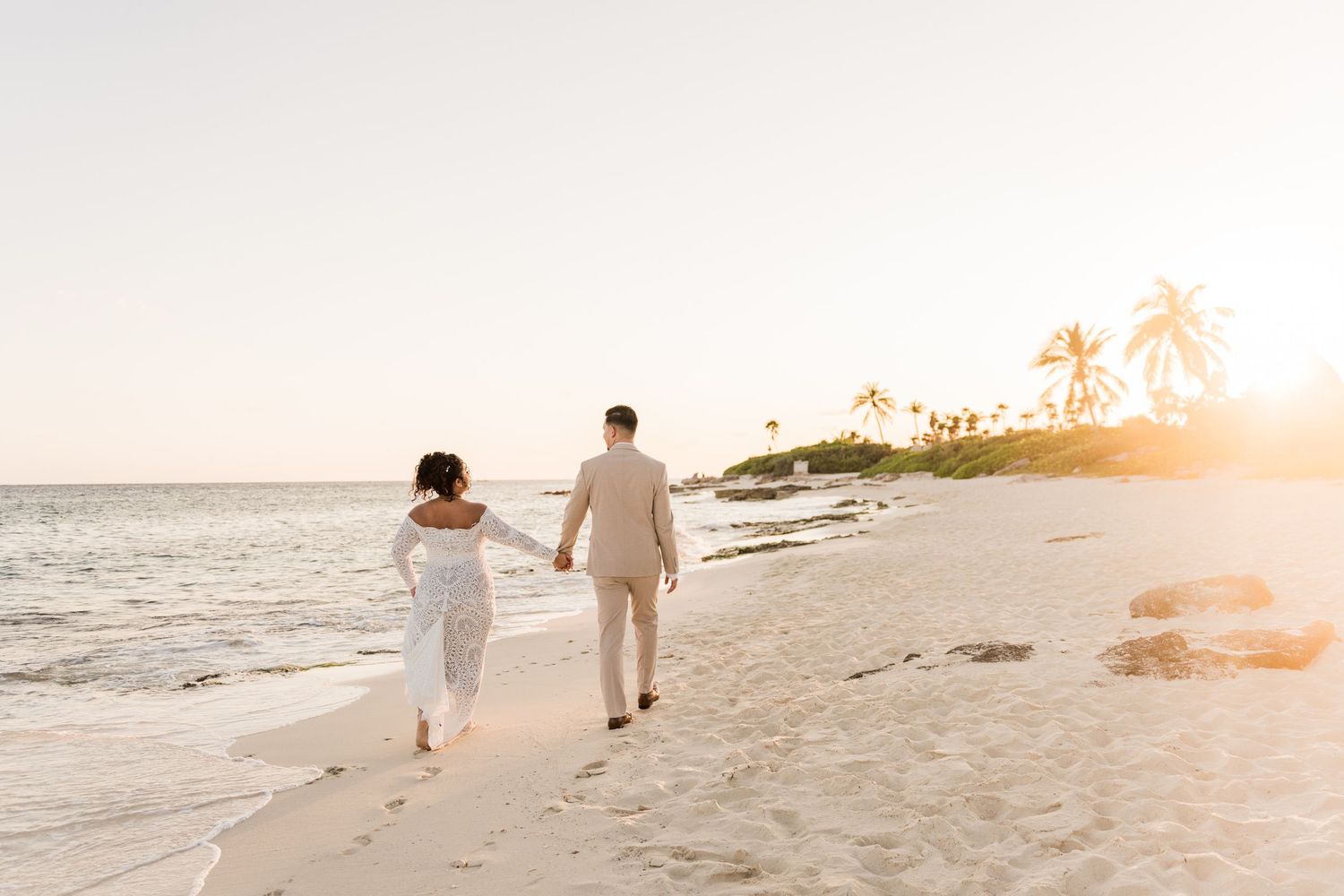 Couple holding hands walking along a tropical beach at golden sunset with palm trees in the background. Puerto Vallarta wedding photographer