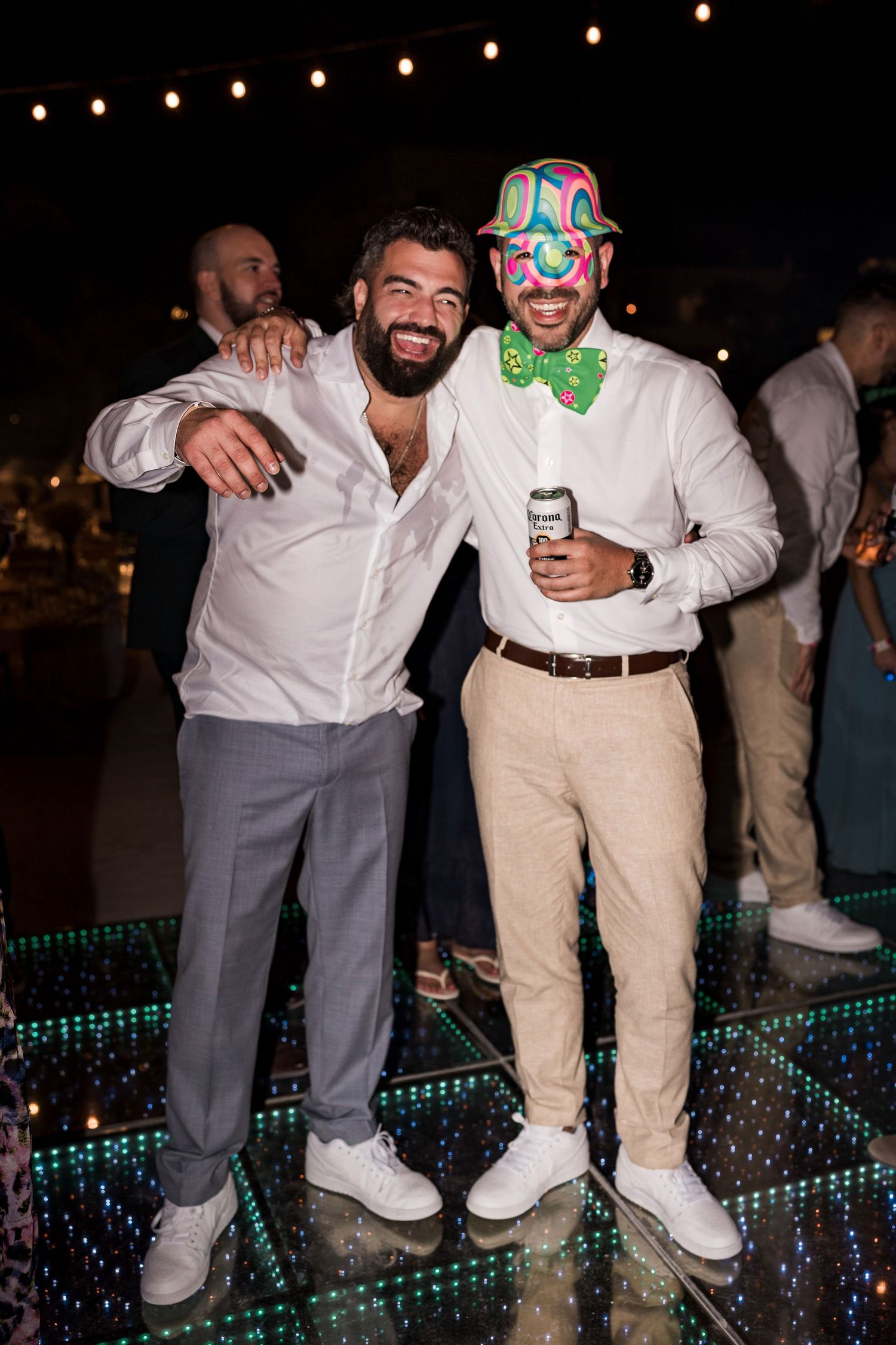 Two men in white shirts smiling and posing together on a dance floor at an outdoor evening party.