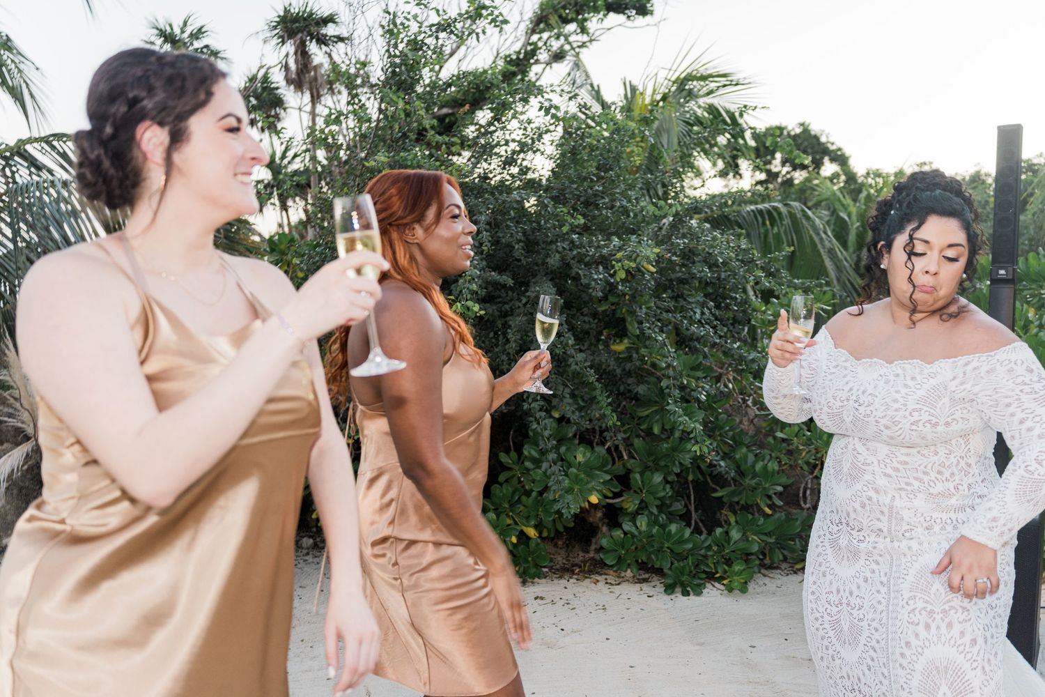 Xcaret Arte Wedding - Bridesmaids in gold dresses toast with champagne alongside bride in white gown at outdoor beach wedding celebration.